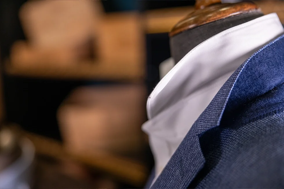 Mannequin portant une veste bleue et une chemise blanche, en arrière-plan des bacs en argile.