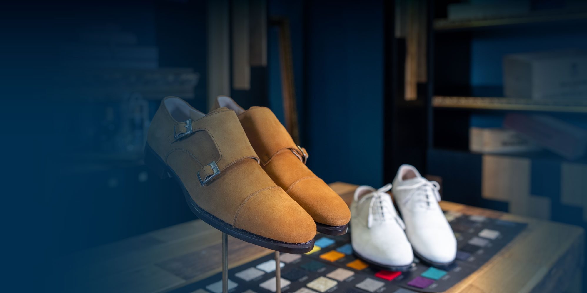 Chaussures en daim beige et marron sur un support en magasin, avec des chaussures blanches en arrière-plan, dans une boutique de chaussures.