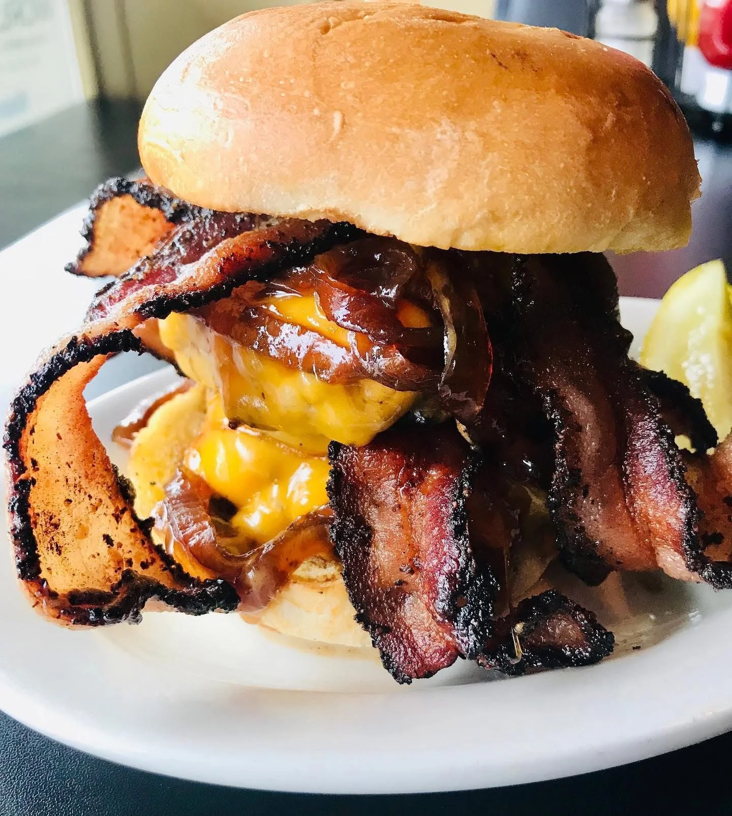 Close-up of a bacon cheeseburger with crispy bacon, melted cheese, and bacon strips in a bun on a white plate.