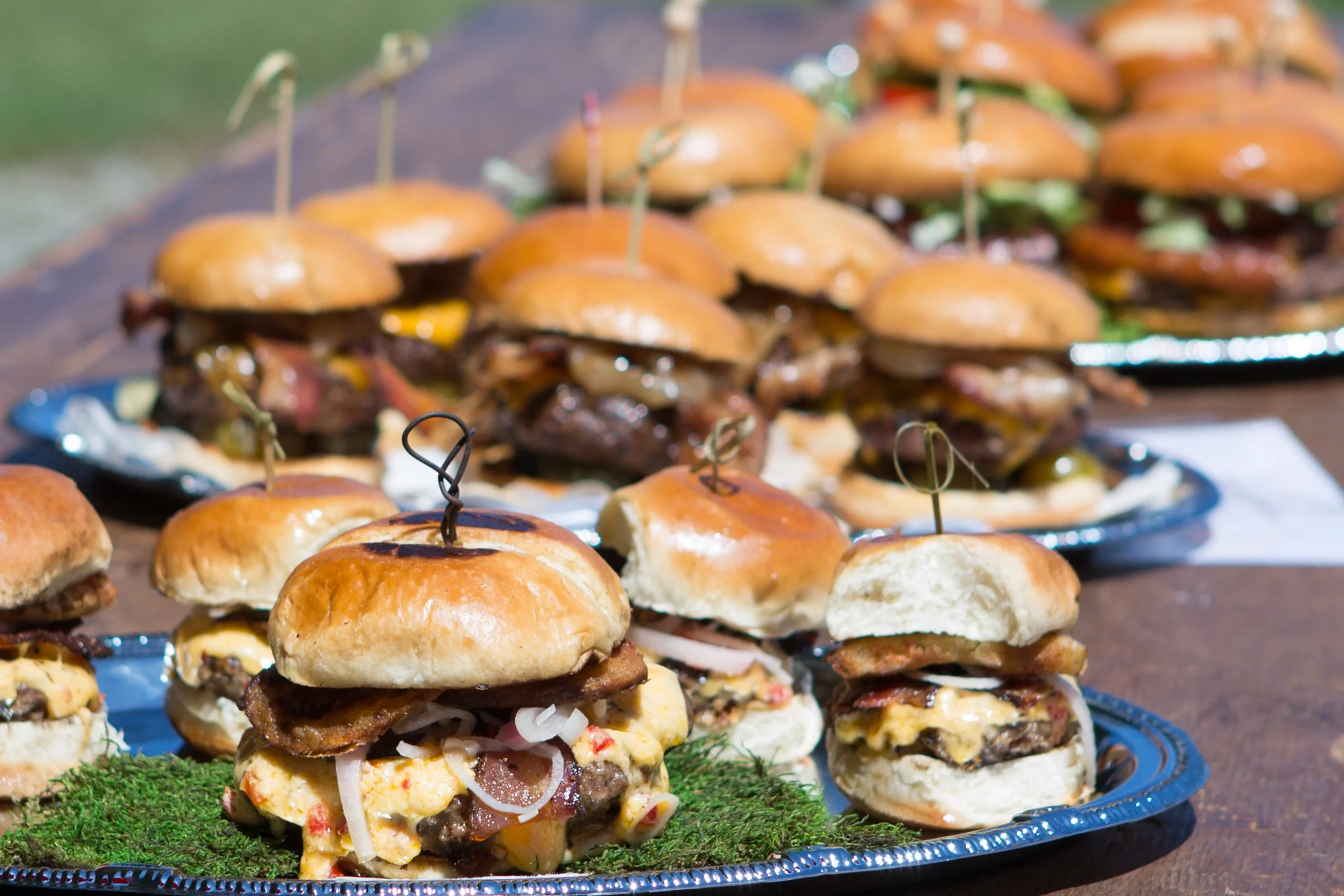 Tray of mini sliders with buns, meat, cheese, onions, and vegetables.