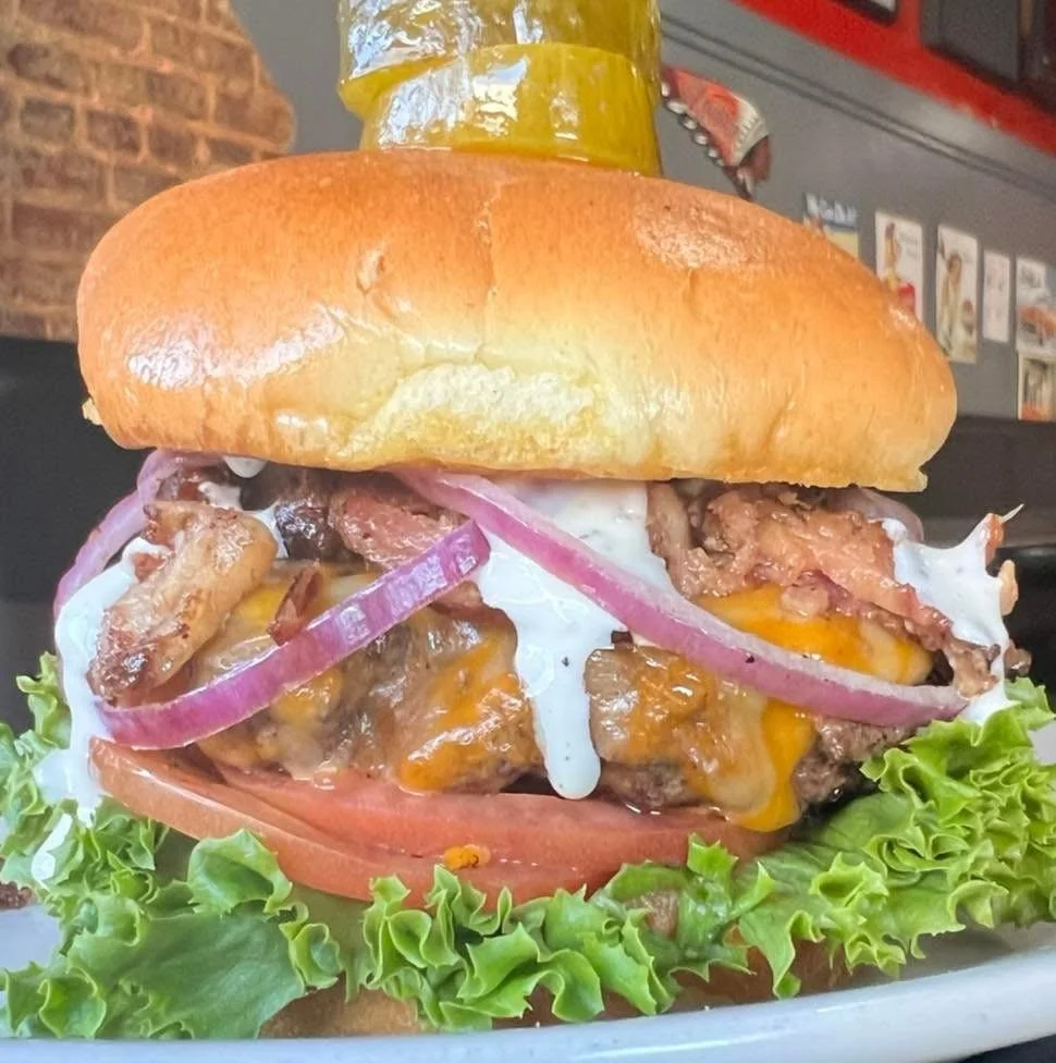 A cheeseburger with bacon, ketchup, onions, tomatoes, lettuce, and a fried egg on a toasted bun.