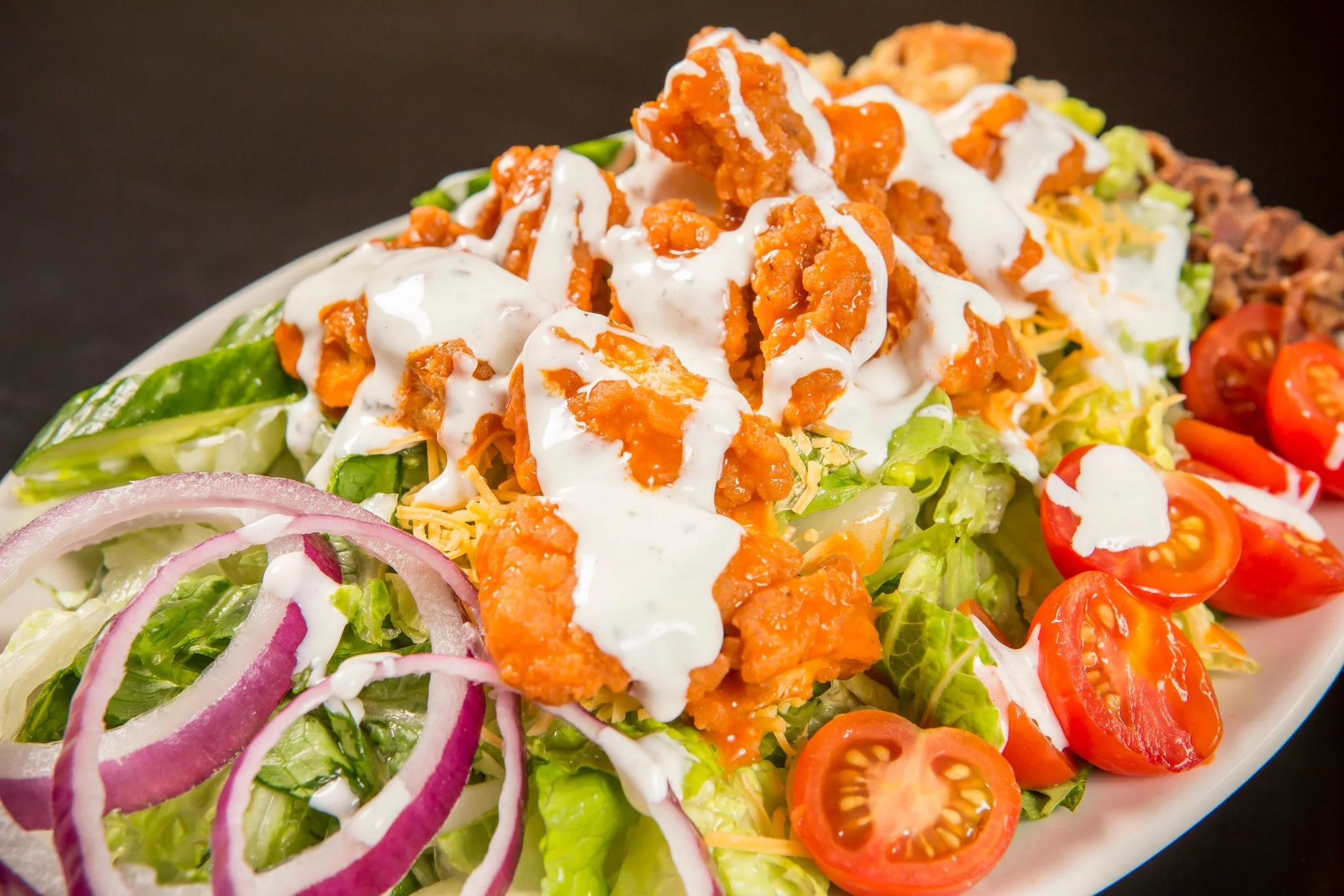 Salad with lettuce, sliced red onions, cherry tomatoes, shredded cheese, chicken with orange sauce, and drizzled dressing.