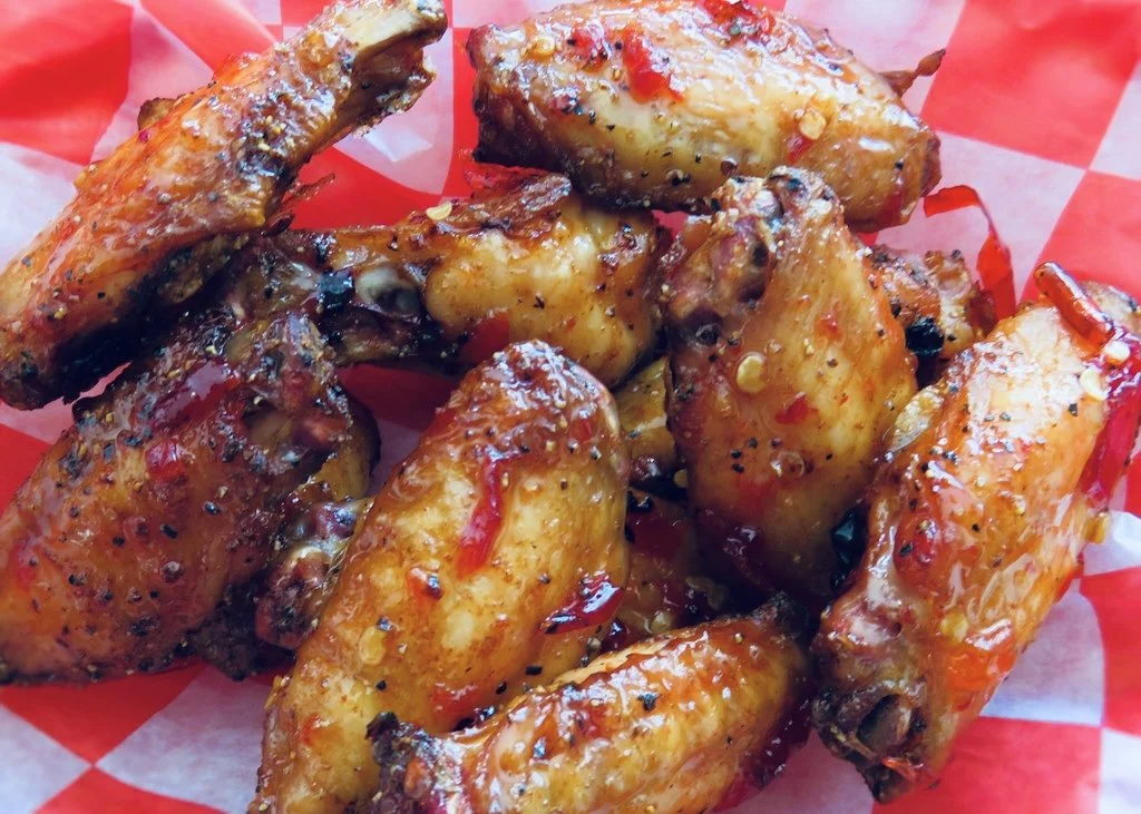 Close-up of glazed, seasoned chicken wings on red and white checkered paper.