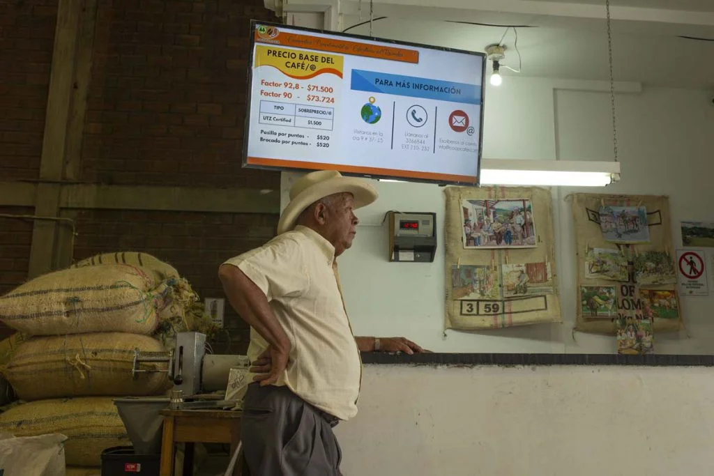 A farmer waits for their pay in the Marsella cooperative for their coffee harvest. While they wait, a screen shows the fluctuating coffee price in real time. Photo: Juan Páez.