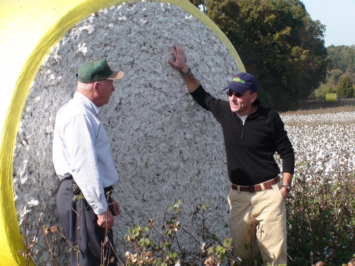 Eric (right) leans on a cotton bale while chatting with a local farmer about the year’s harvest.