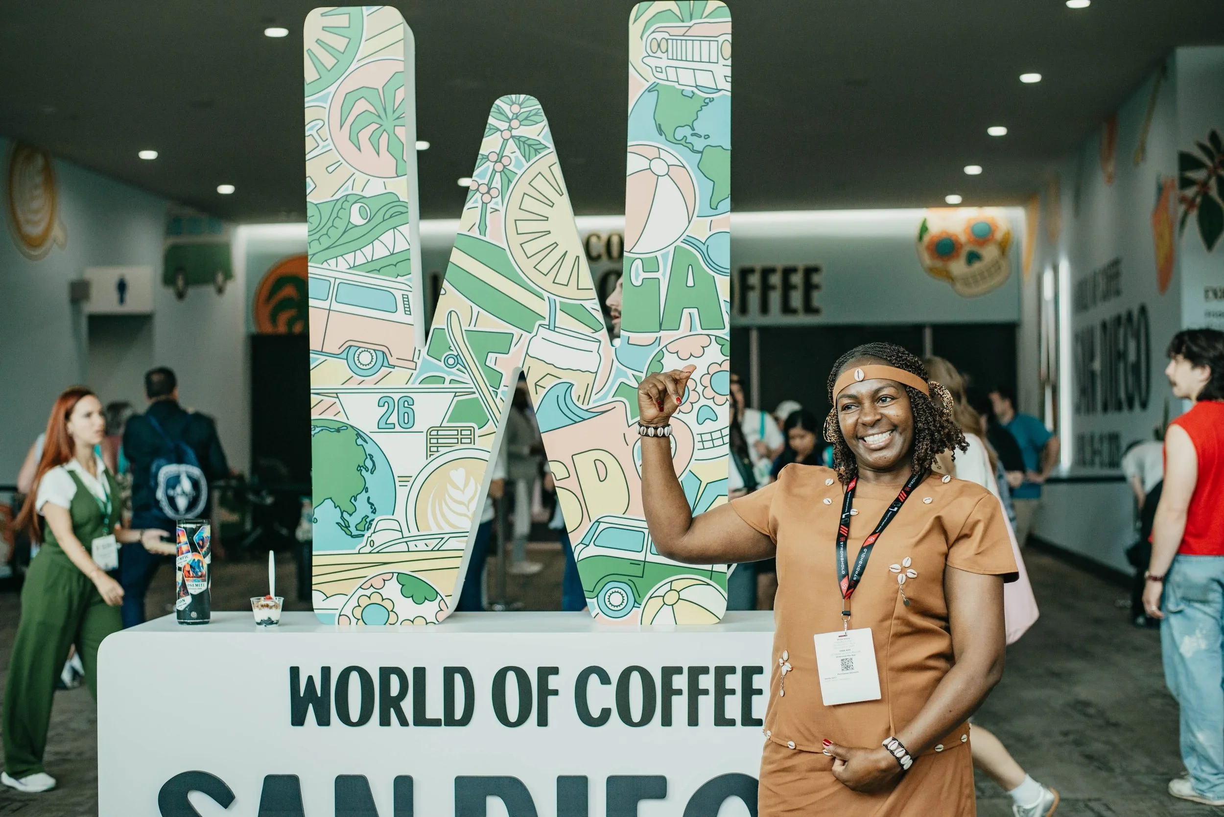 Person smiling while standing in front of a World of Coffee San Diego three dimensional sign
