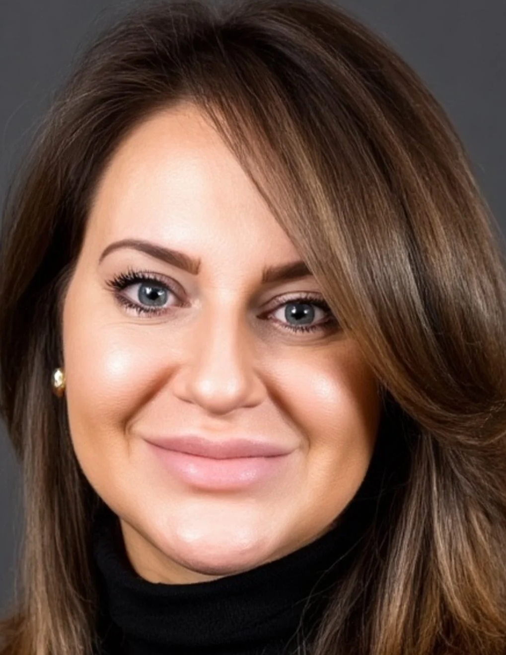 Close-up of a woman, Mary-Jo Lake, with brown hair, blue eyes, and a black turtleneck, smiling against a dark background.
