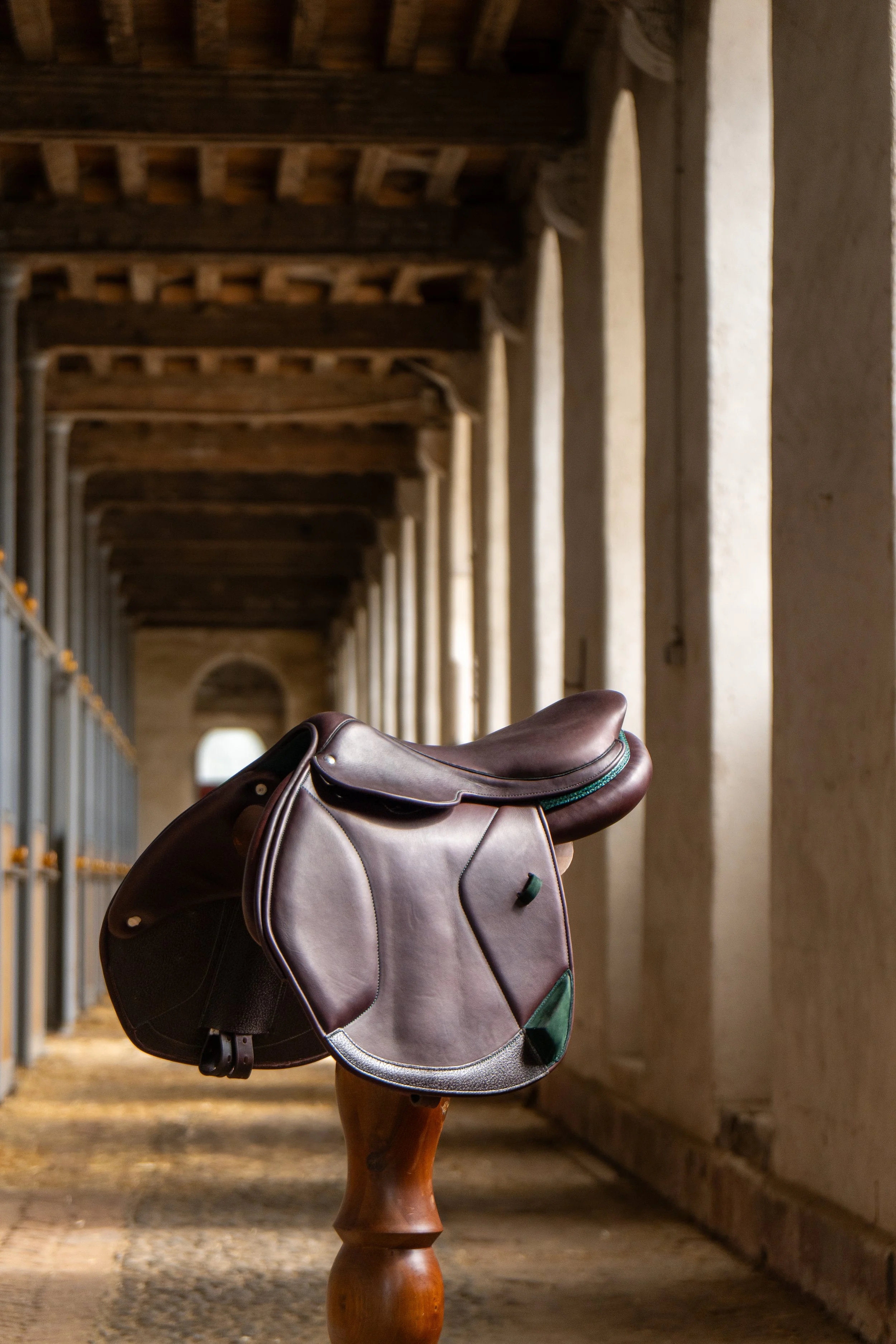 Une selle de cheval posée sur un support en bois dans une gliserie en pierre avec des arches en fond.