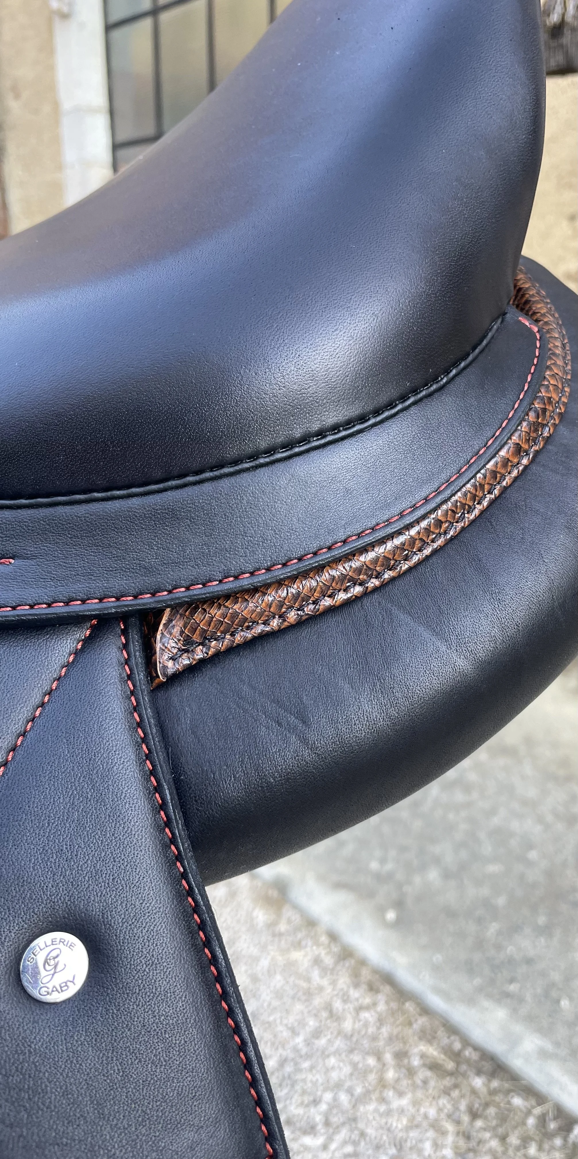 Selle de cheval en cuir noir avec détails en cuir tressé marron et couture rouge.