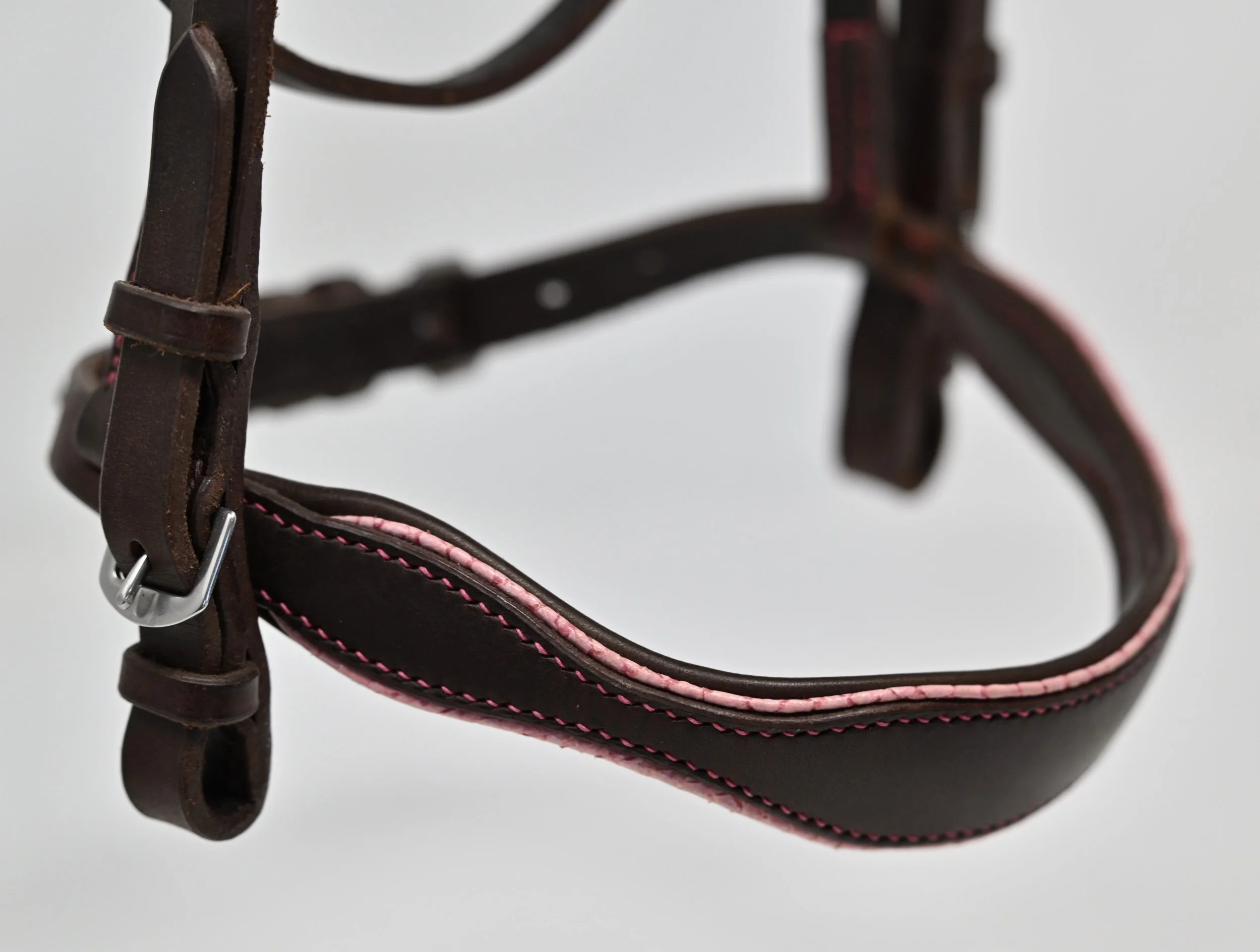 Un filet pour cheval en cuir marron avec une finition en rose, vue de côté.