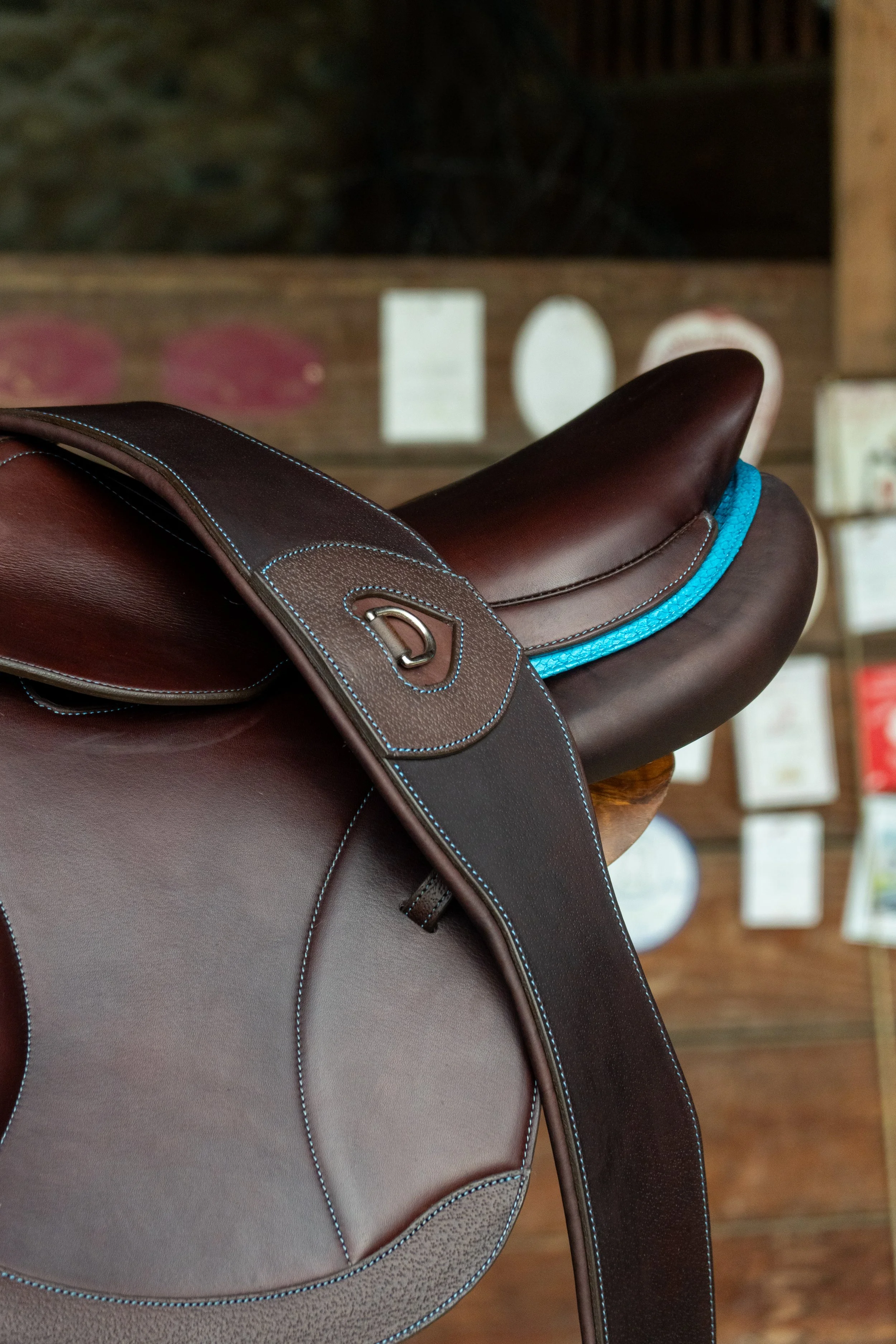 Une selle de cheval marron avec des coutures bleues et une bride en cuir, posée sur un support en bois.