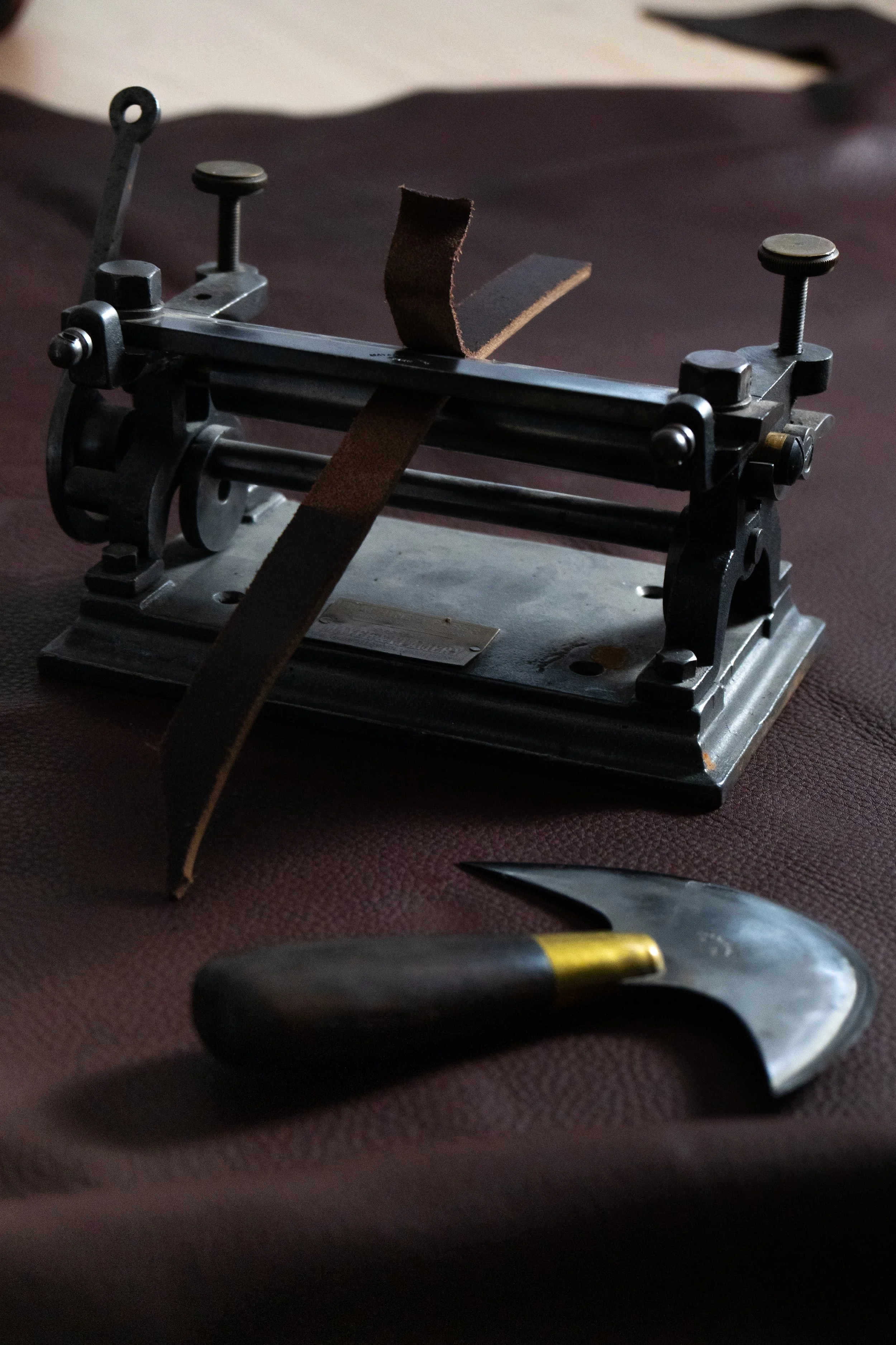 Une balance à bagages ancienne avec une bande de cuir, une pince, un couteau et une pierre à aiguiser sur une surface en tissu marron.