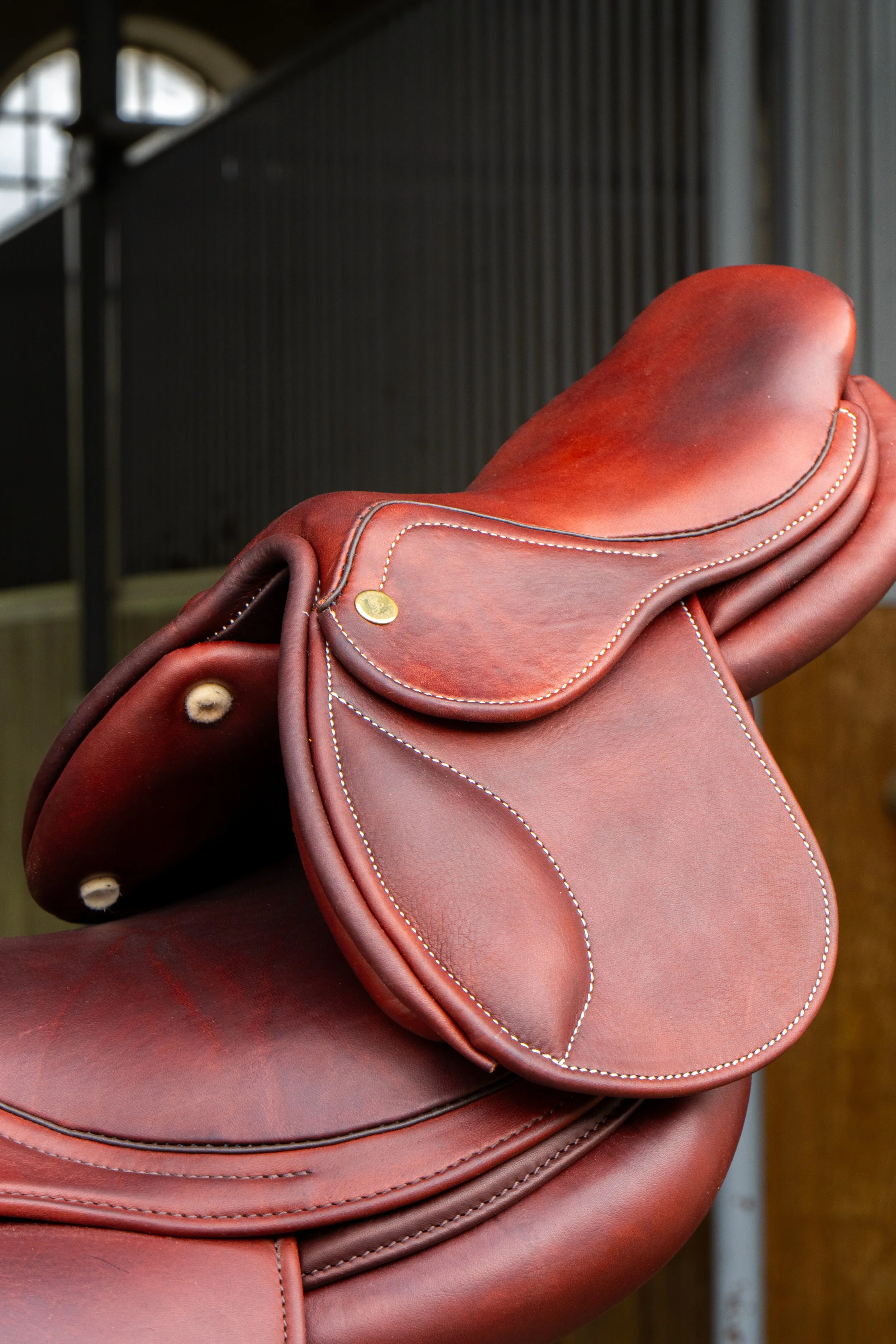 Une selle de cheval en cuir marron avec des coutures blanches, fixée à un cheval, dans un environnement intérieur ou une écurie.