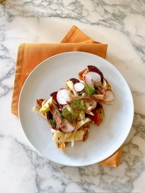 A plate of salad with radish slices, and sliced meat on a white plate, placed on a marble surface with an orange napkin underneath.