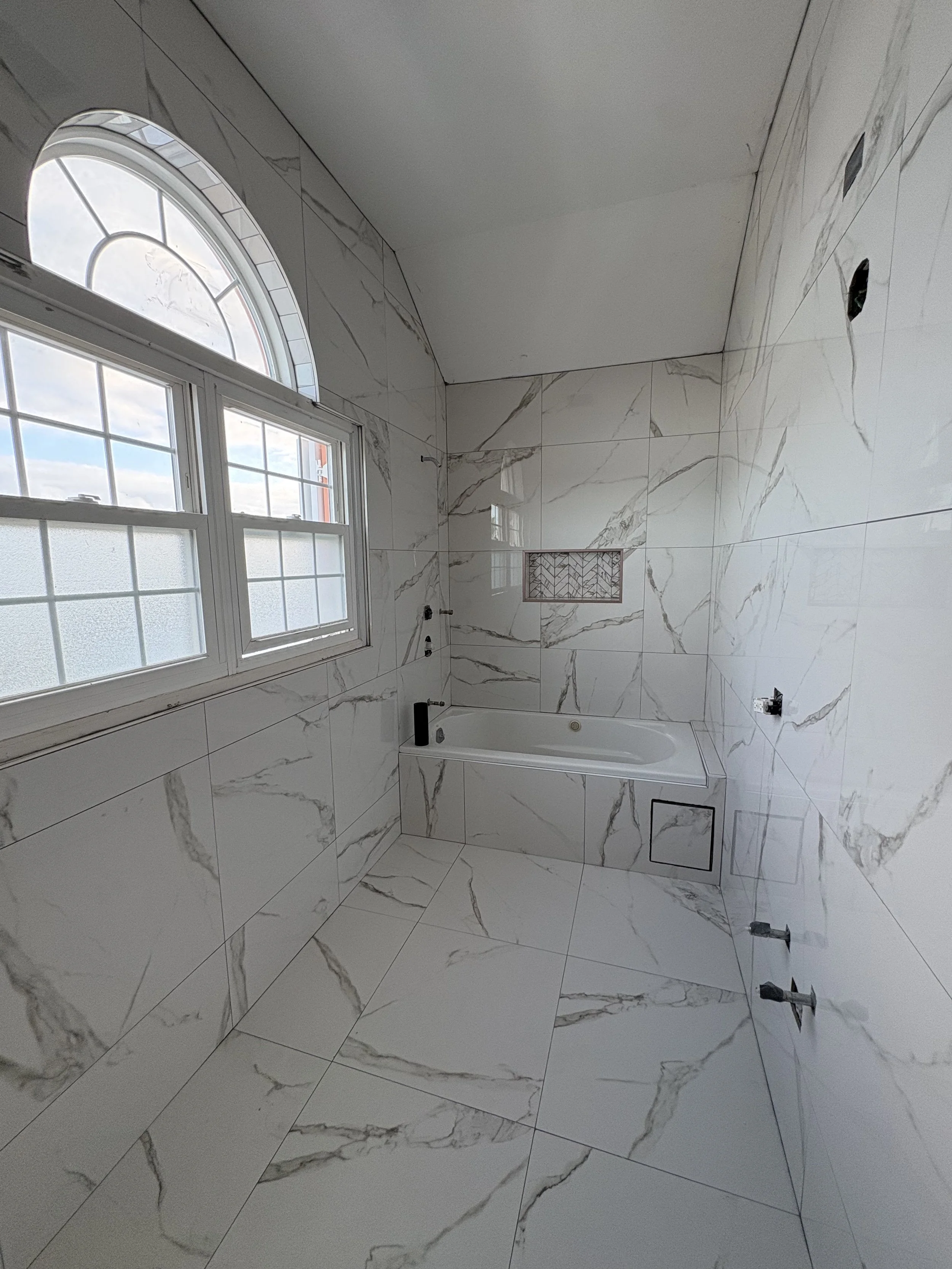 A bathroom under construction with marble tile walls and floor, a bathtub, and no fixtures installed yet.