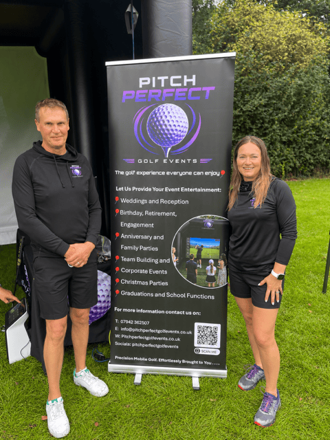 Mick and Mandie Percival business owners standing outdoors next to a Pitch Perfect Golf Events banner, which advertises golf event services for various occasions, with trees and grass in the background.