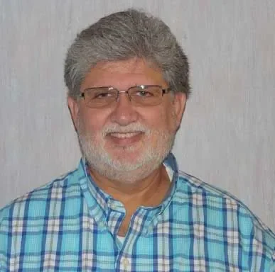 A middle-aged man with gray hair and a beard, wearing glasses and a blue plaid shirt, smiling at the camera.