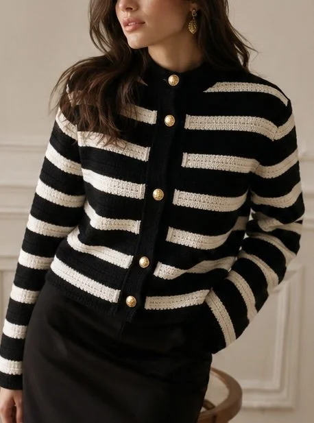 Femme portant un cardigan noir et blanc rayé avec des boutons dorés et une jupe noire, en intérieur.