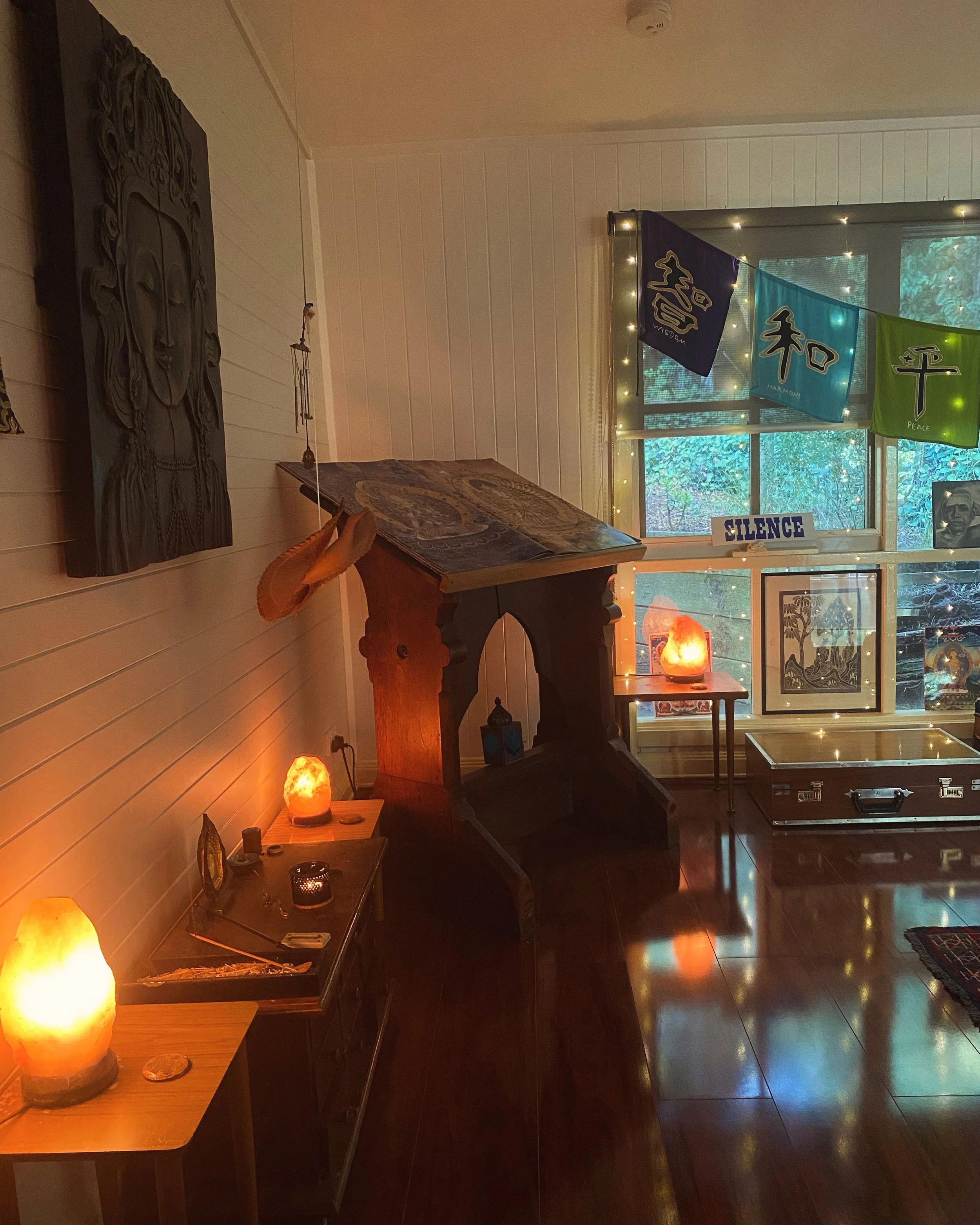 A cozy room decorated with spiritual and artistic items, featuring a Himalayan salt lamp, artwork, and colorful prayer flags hanging near a window with fairy lights, creating a peaceful and calming atmosphere.
