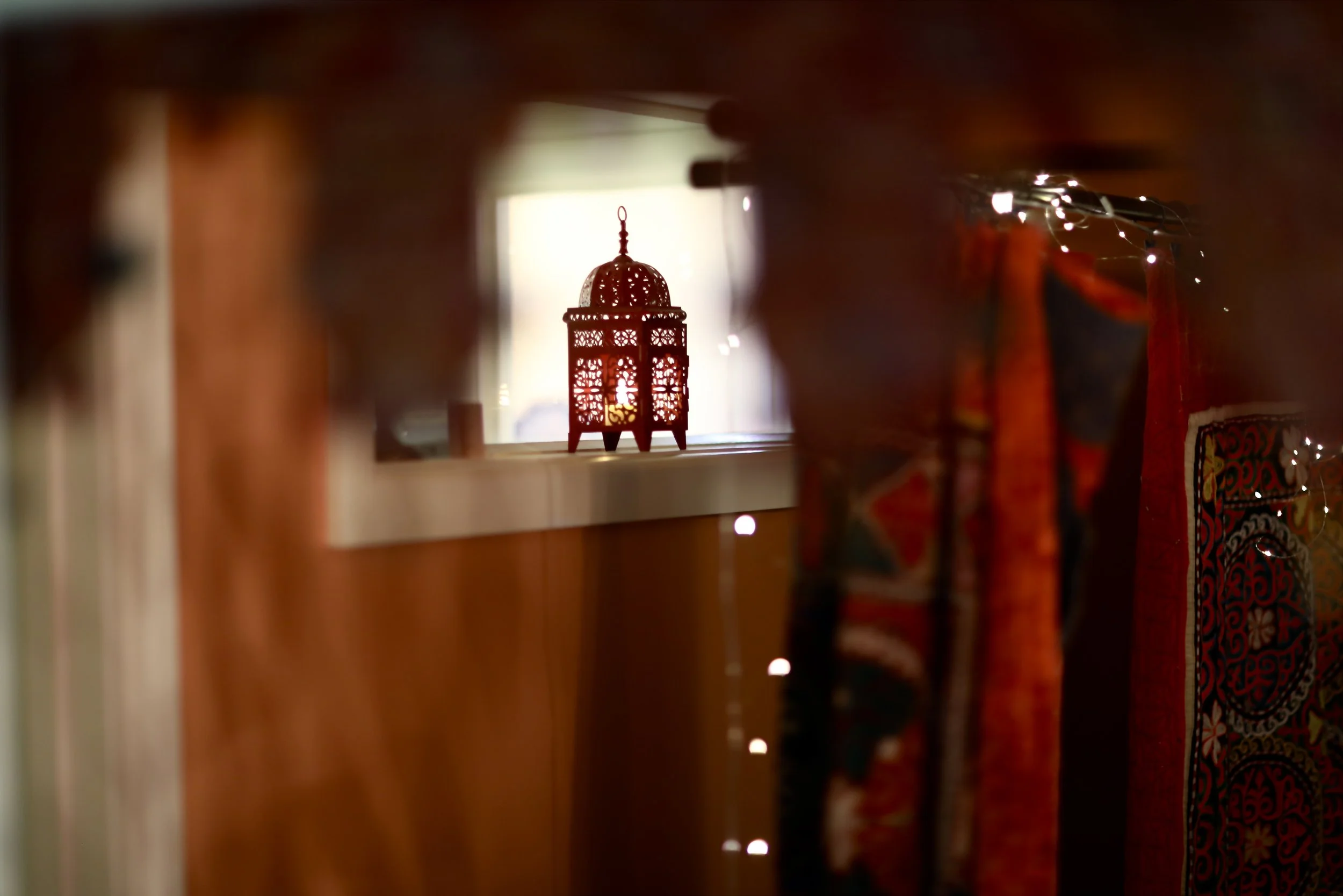 A decorative lantern placed on a shelf with a lit candle inside, viewed through a small opening with curtains on the right side.