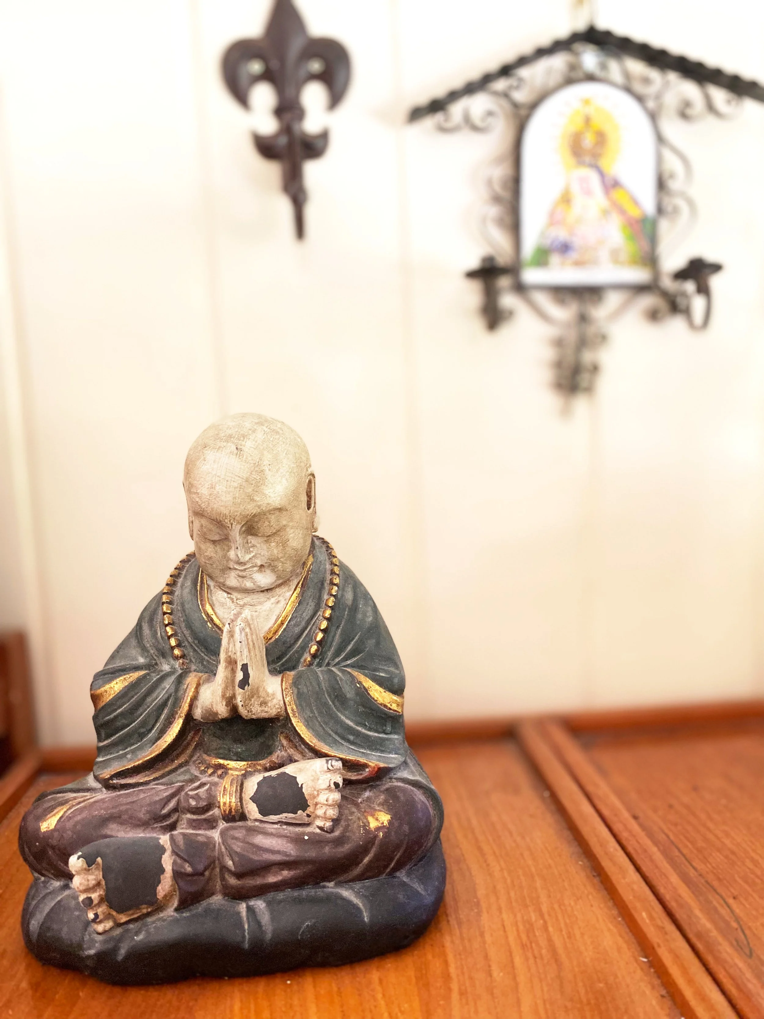A small statue of Buddha in a meditative pose, with hands pressed together in prayer or greeting, sitting on a wooden surface.
