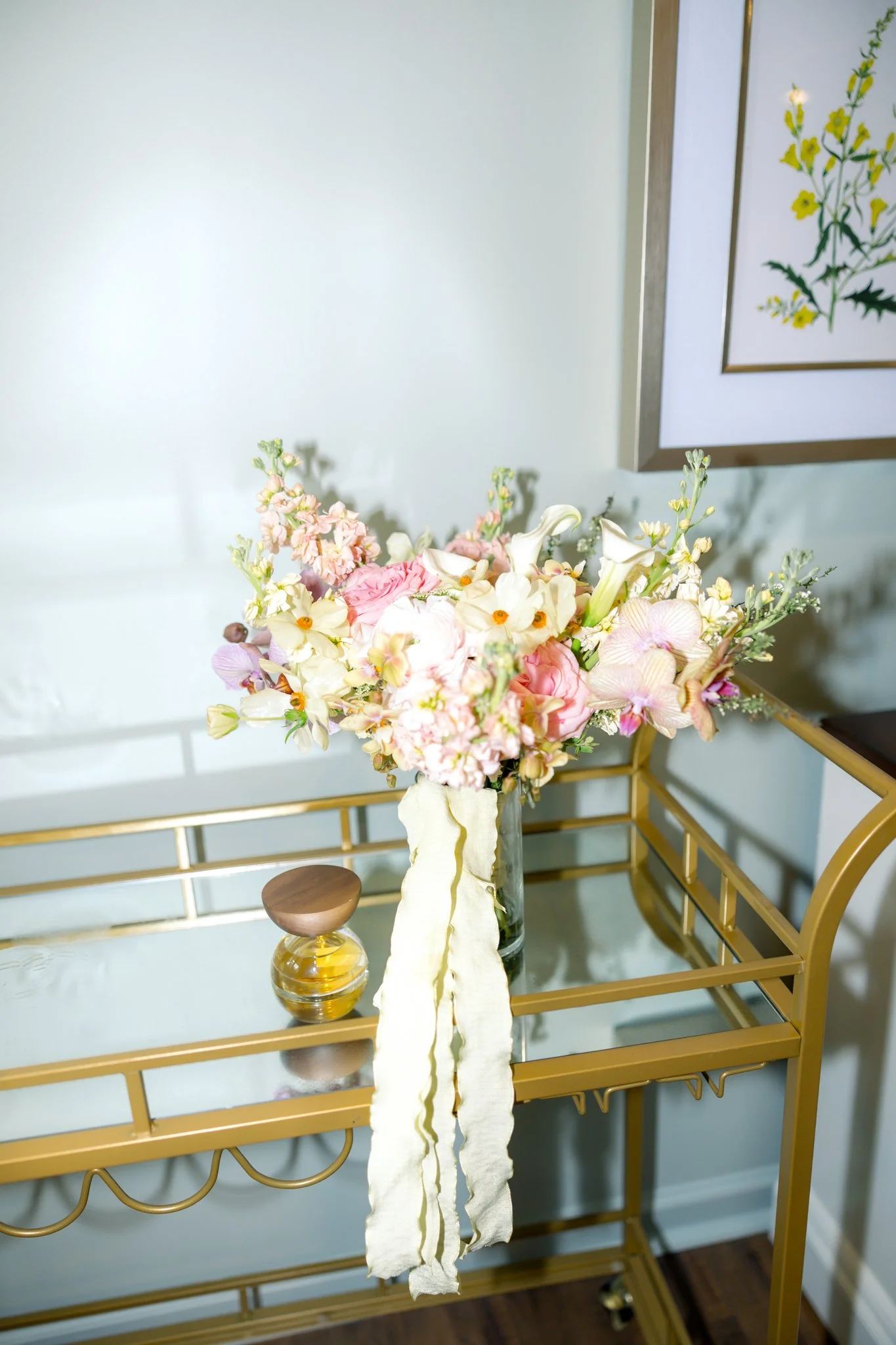 A floral arrangement featuring pink and white flowers on a gold table with a small glass vase underneath.
