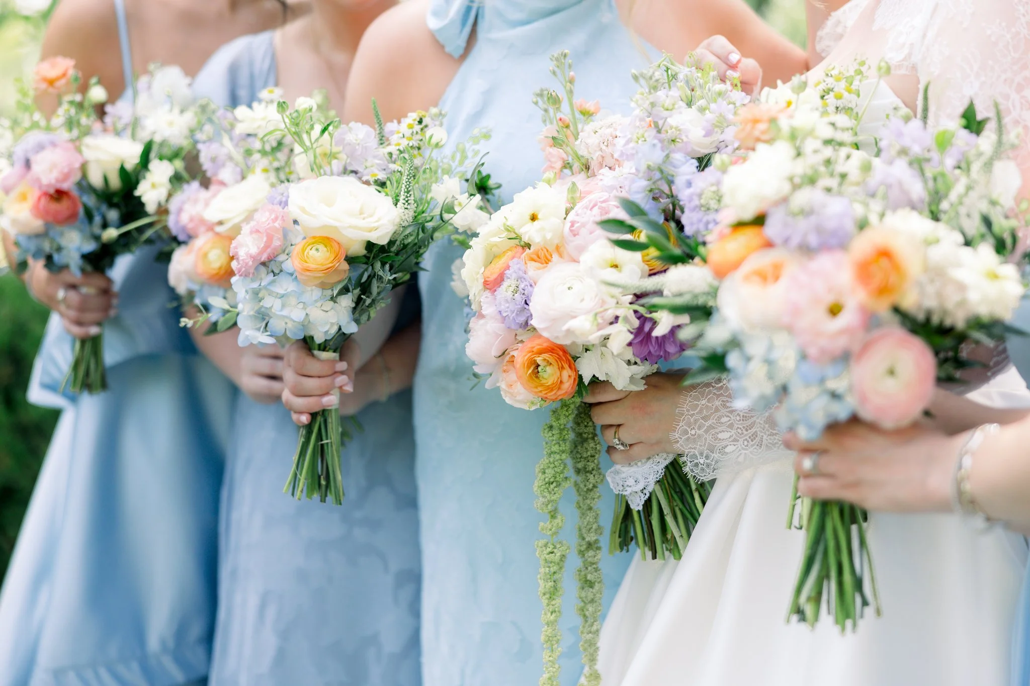 Close-up of women holding colorful flower bouquets, likely at a wedding or celebration outdoors.