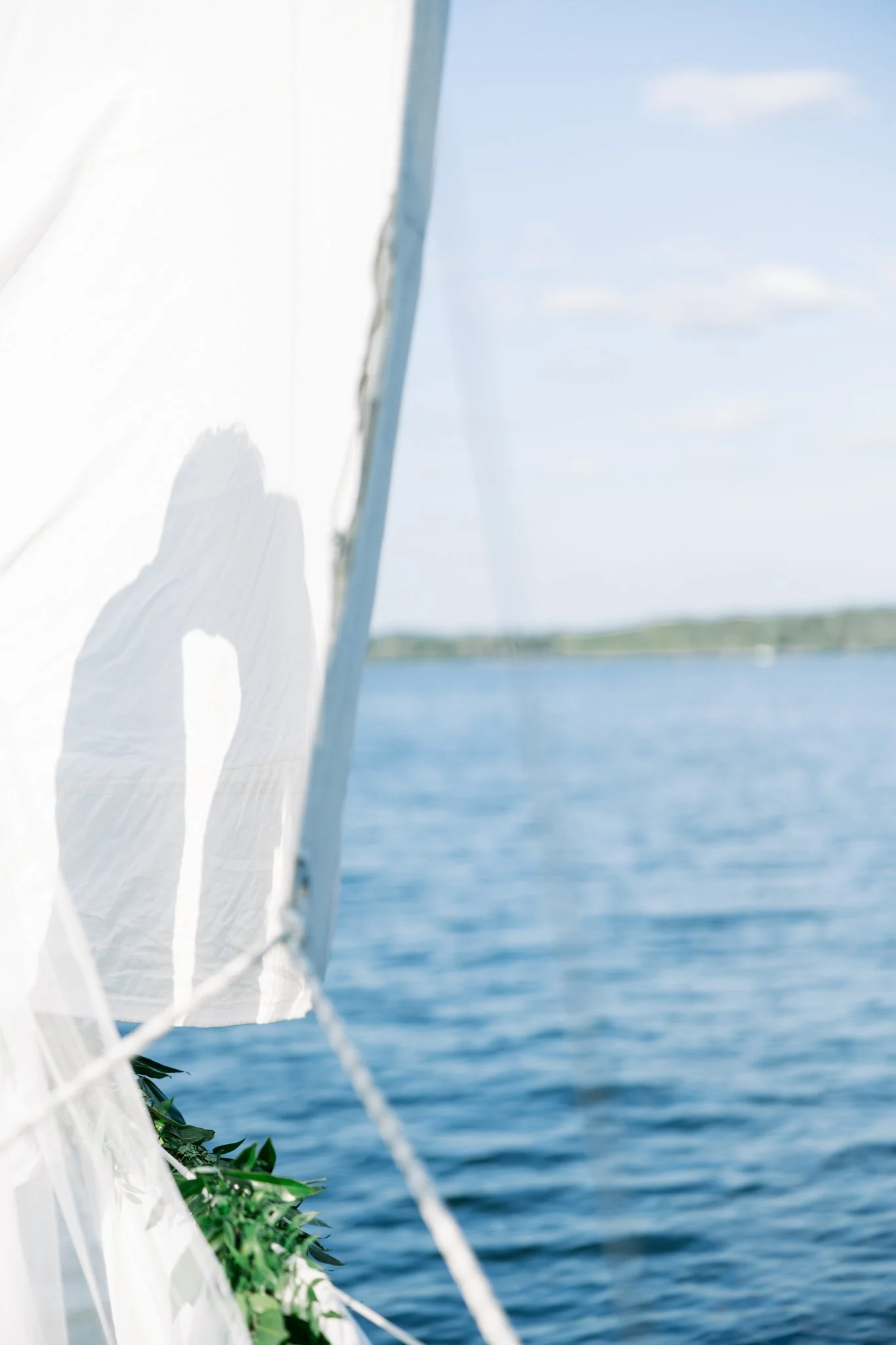A white fabric or paper with a shadow of a person, positioned next to a railing on a boat, with water and a clear sky with some clouds in the background.
