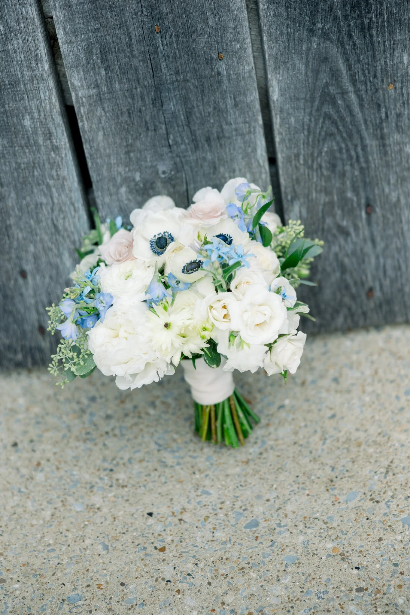 A bouquet of white and blue flowers resting against a dark wooden fence.