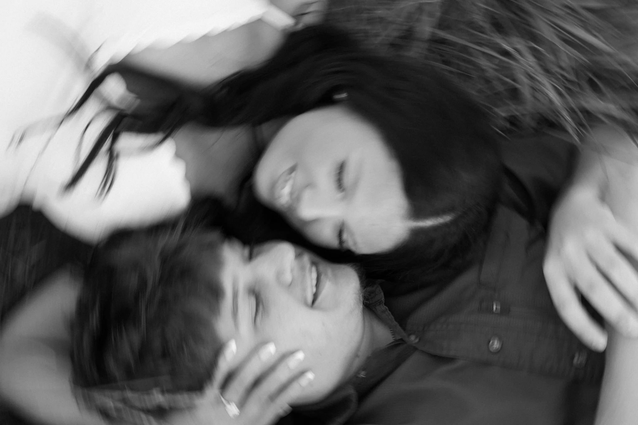 A woman with long dark hair lies on her side with her eyes closed, smiling. She is wearing a dark jacket, and the background is out of focus.