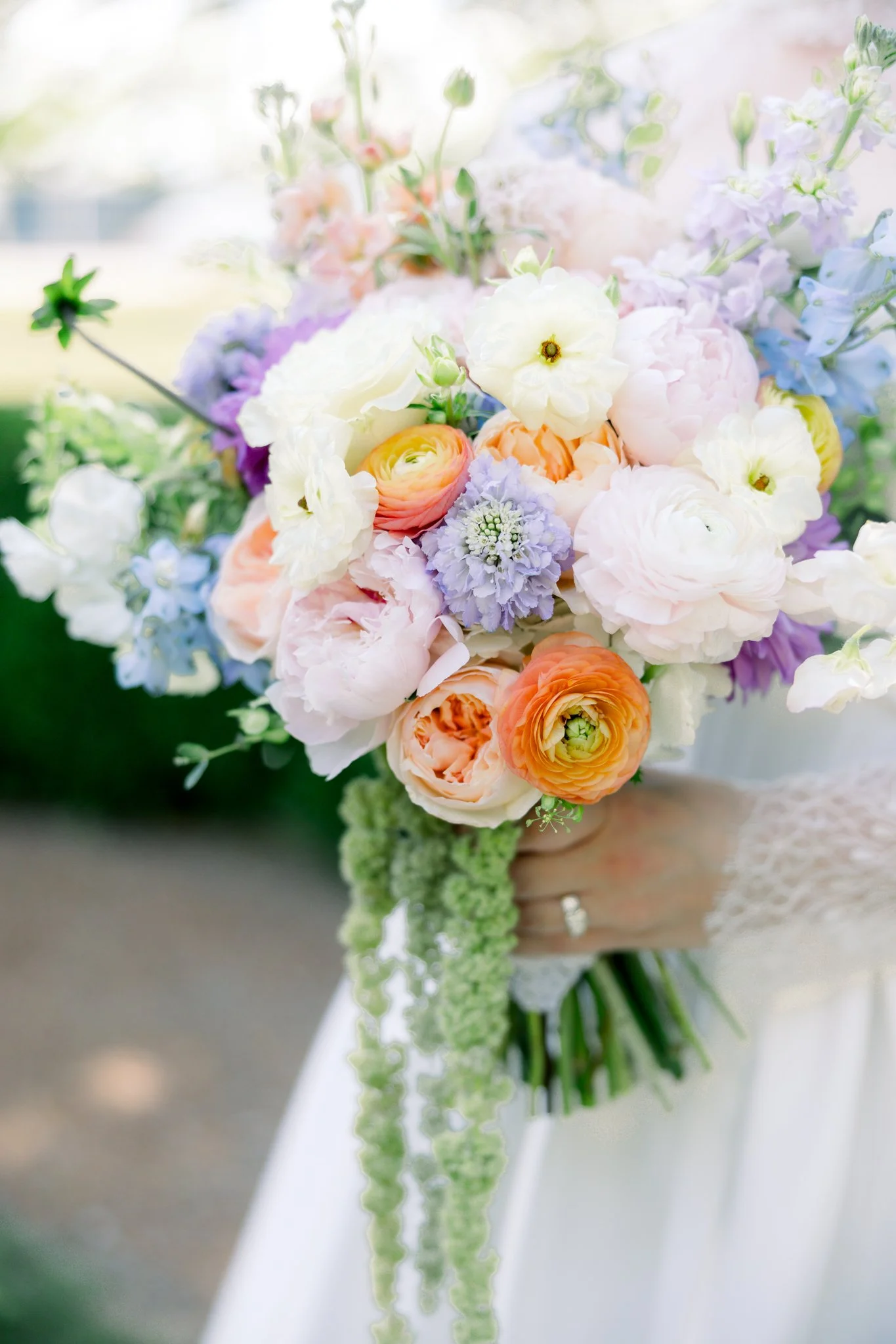 A floral bouquet with white, peach, purple, and blue flowers being held by a person at a wedding or special event.