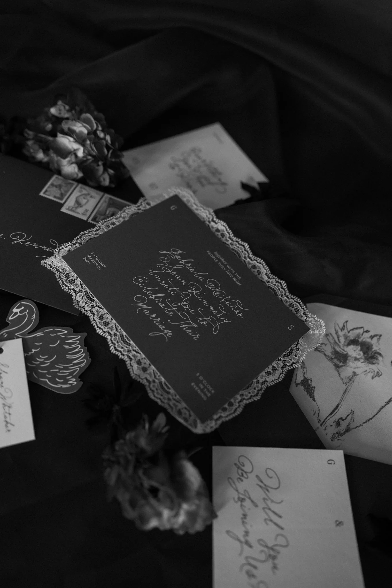 Black and white photo of a wedding invitation, a small bouquet of flowers, and handwritten notes on paper.