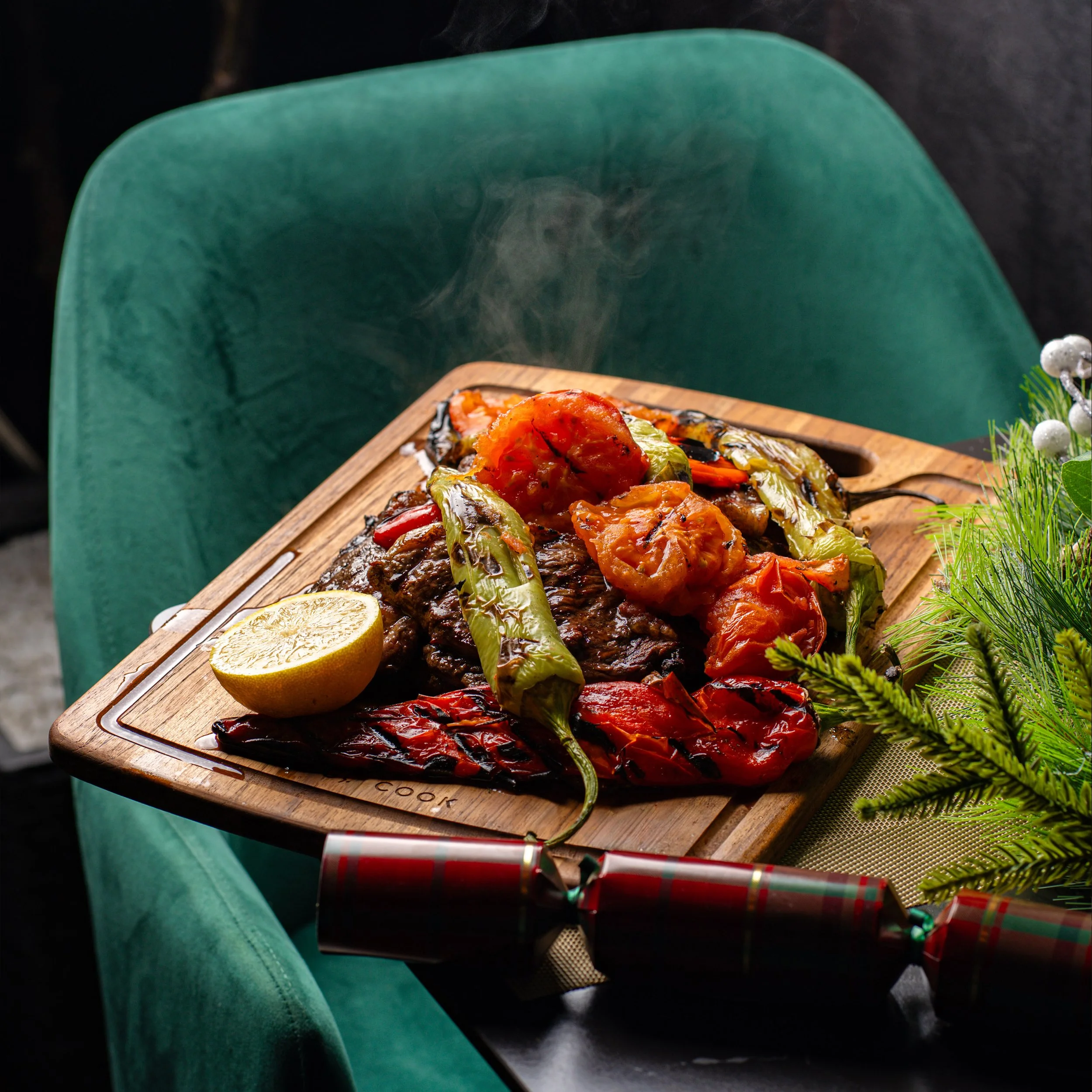 A wooden tray with cooked food, lemon slices, and holiday decorations, resting on a person's lap wearing turquoise pants.