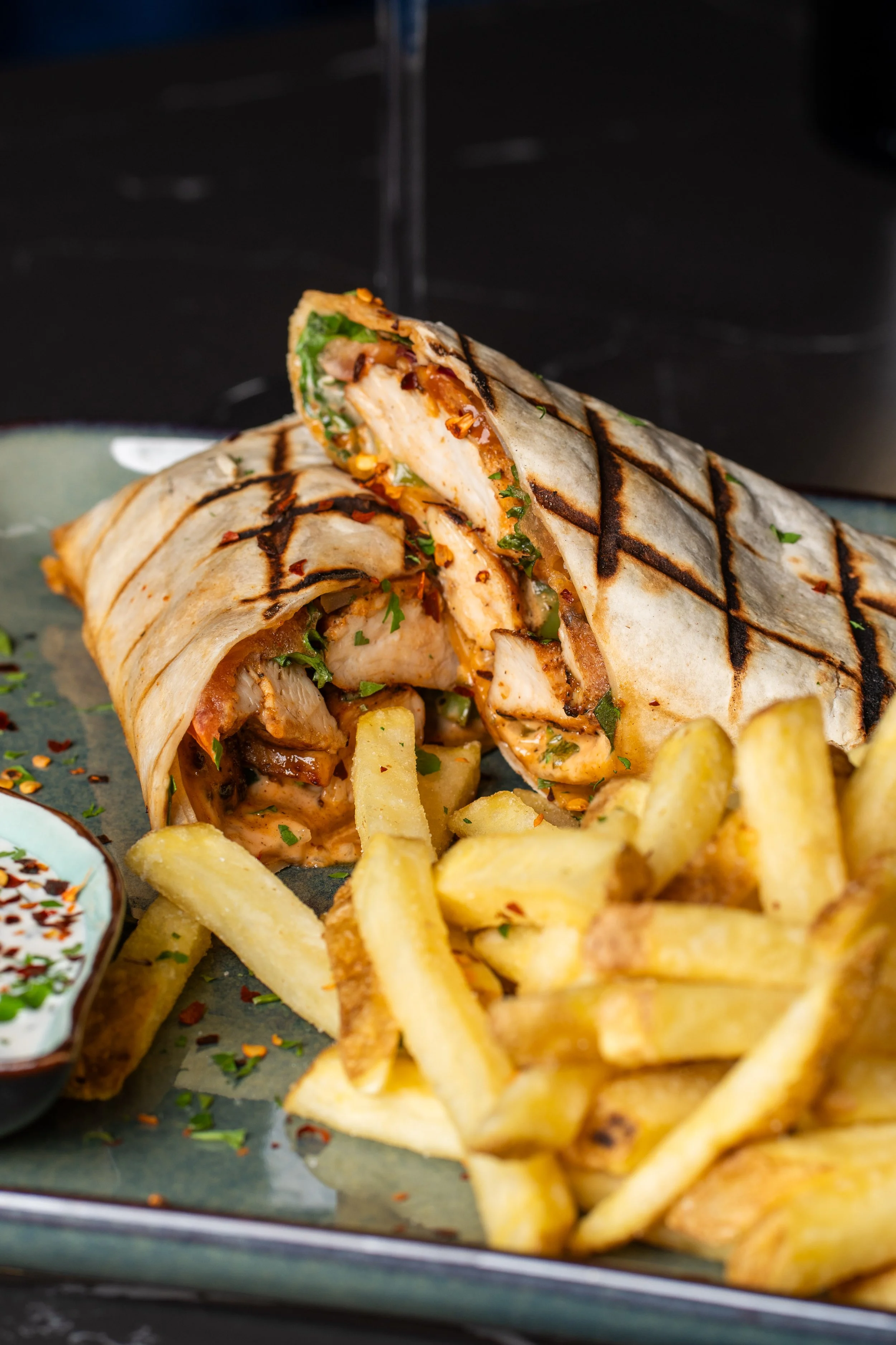 Grilled wrap with chicken, vegetables, and herbs, accompanied by French fries on a plate.