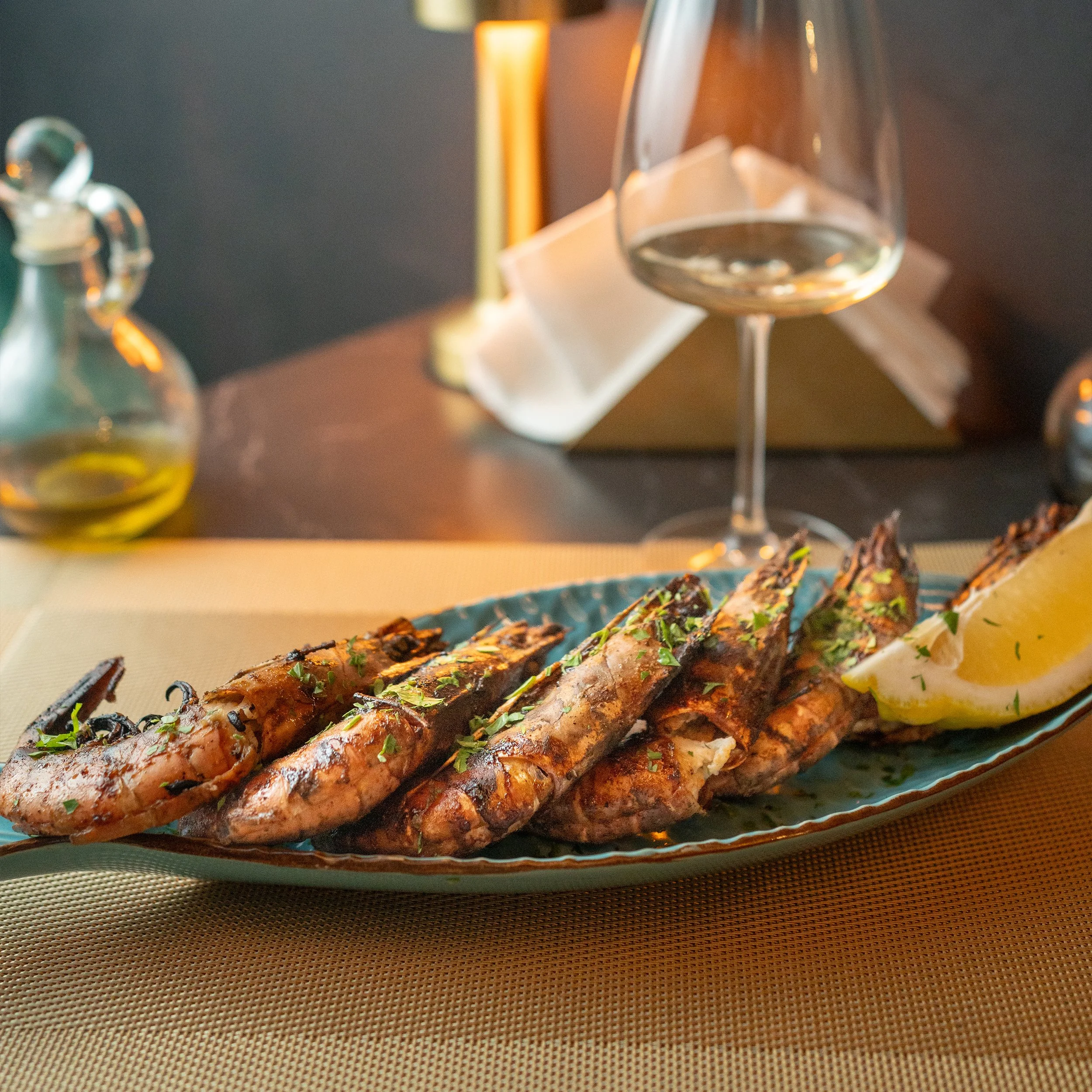 Close-up of grilled fish with herbs served on a plate, with lemon wedges, in a restaurant setting.