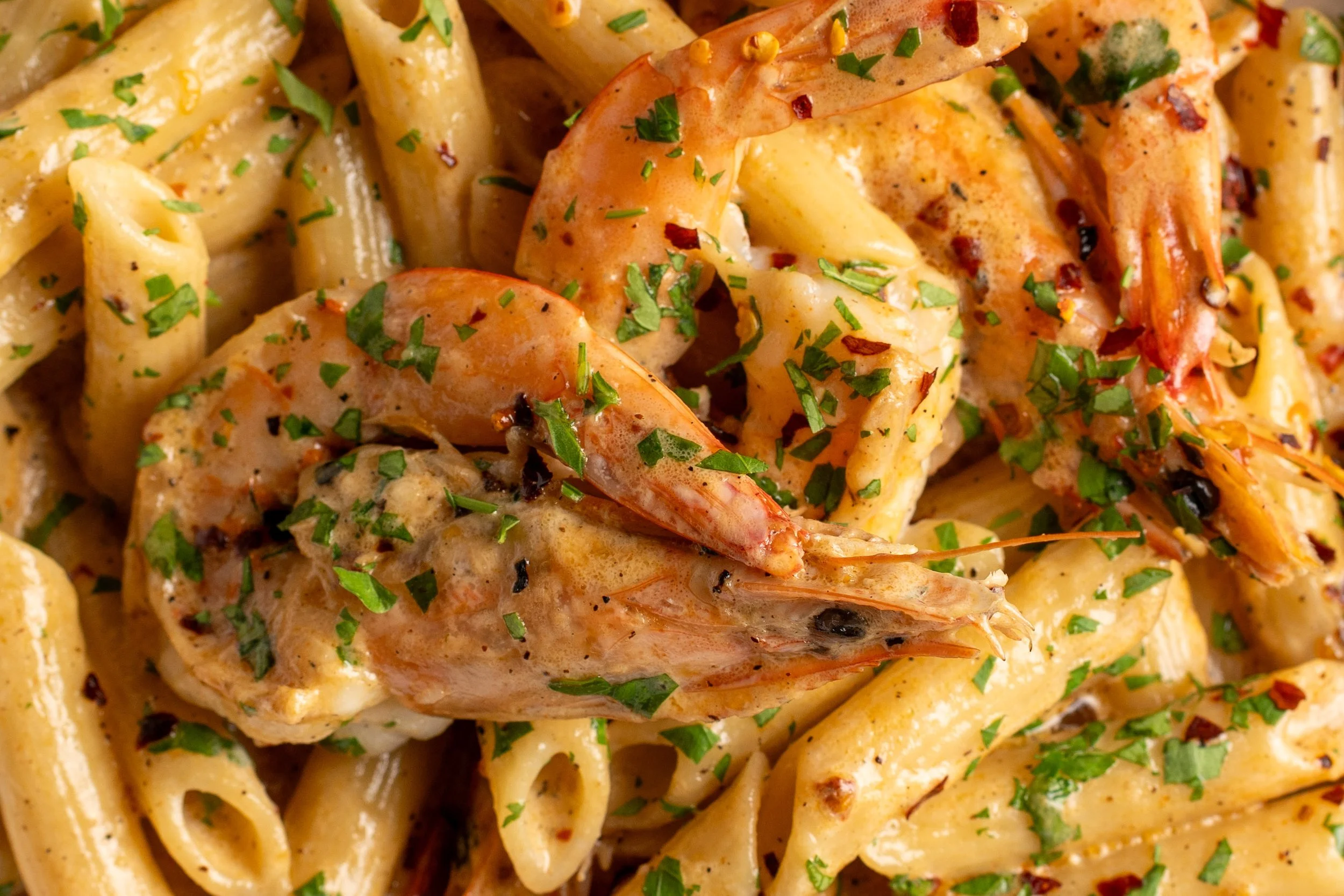 Close-up of cooked shrimp and pasta garnished with chopped herbs.