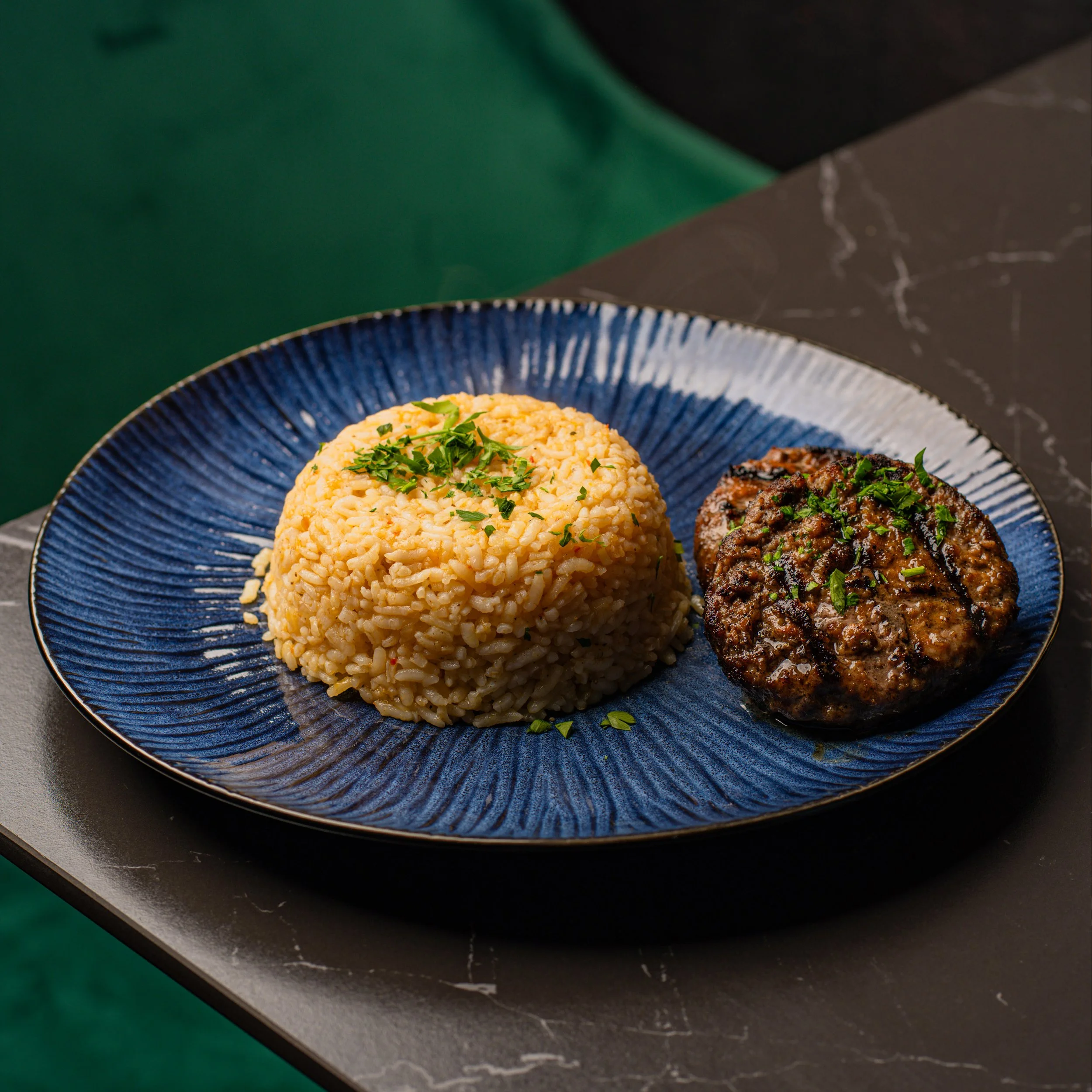 Close-up of a blue ceramic plate with rice, garnished with chopped green herbs, sitting on a dark marble countertop.