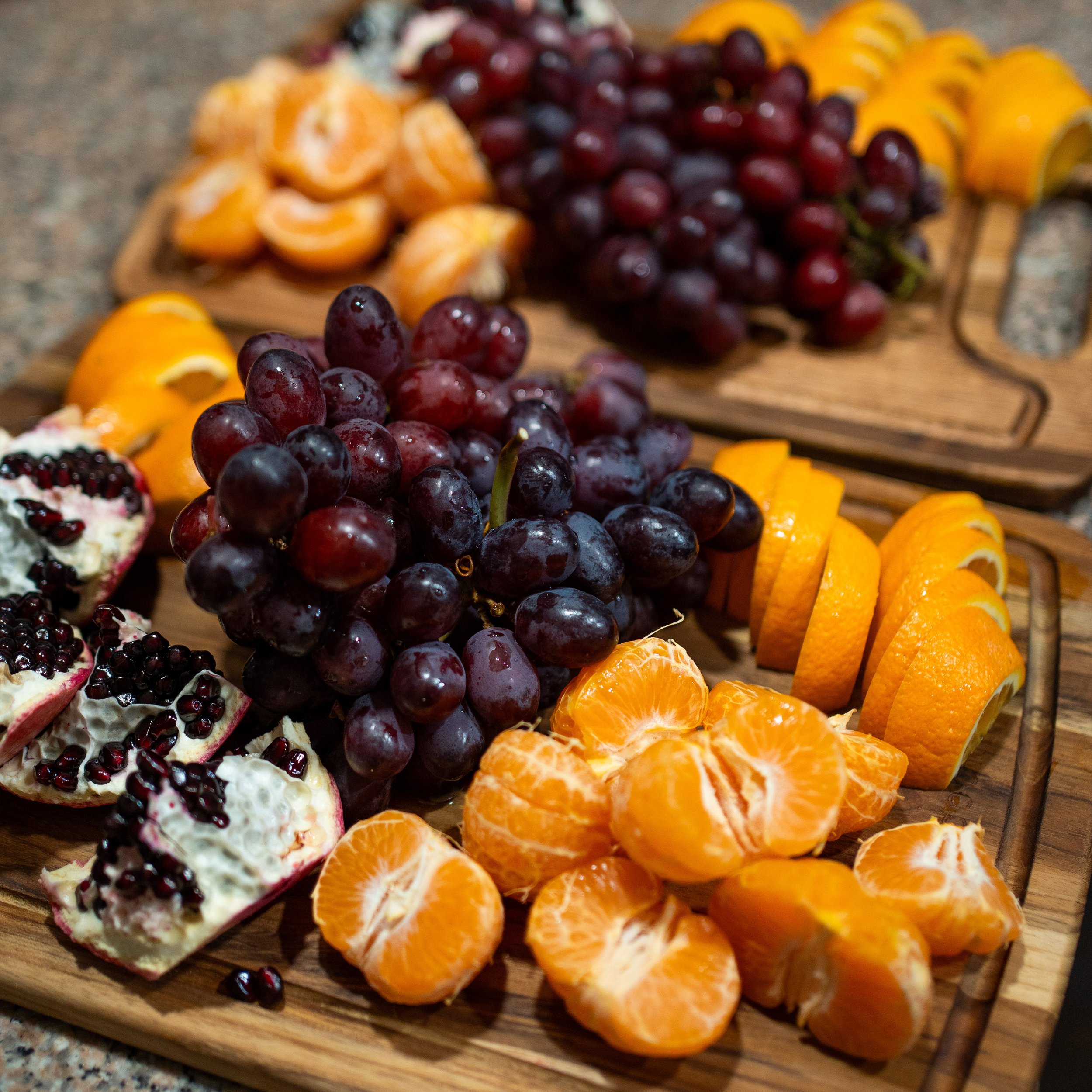 Close-up of assorted sliced fruits on a wooden tray, including oranges, red grapes, and a berry-topped dessert