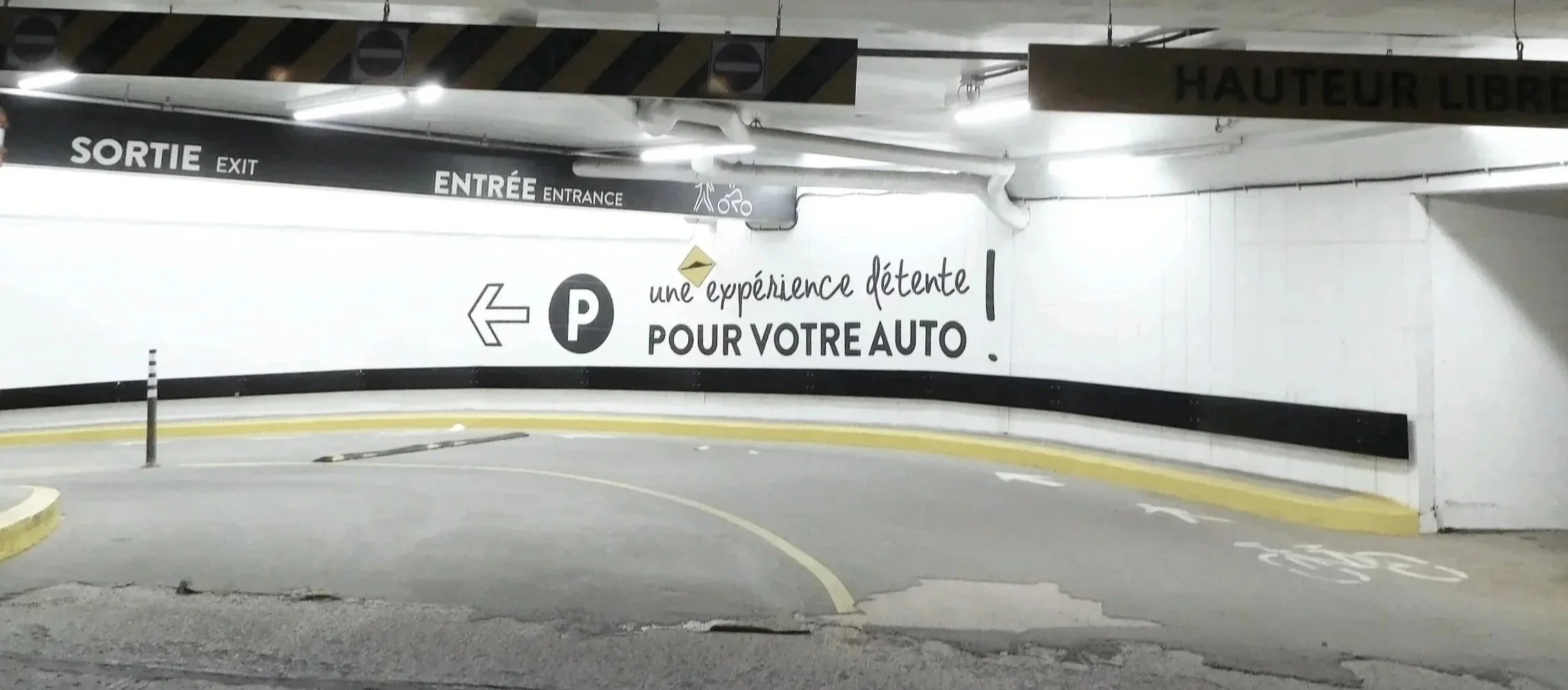 Underground parking garage entrance with signage in French and English, indicating exit and entrance, with parking instructions for autos.