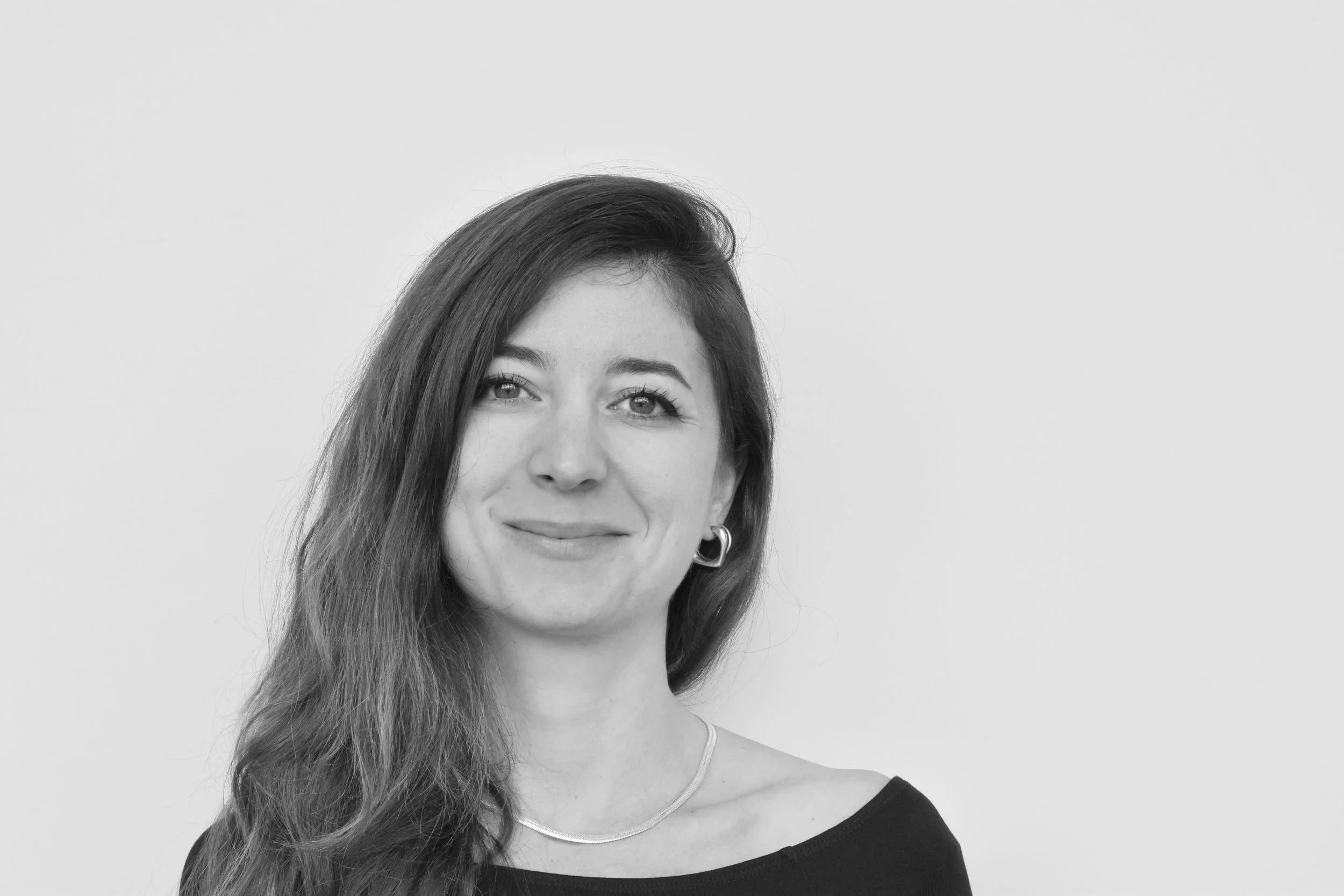 Black-and-white portrait of Stella, founder of eftopia, smiling against a plain background. She has long hair and wears earrings, a necklace, and a black top.