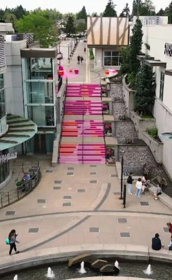 A wide urban pedestrian street with colorful stairs, shops, and people walking and sitting.