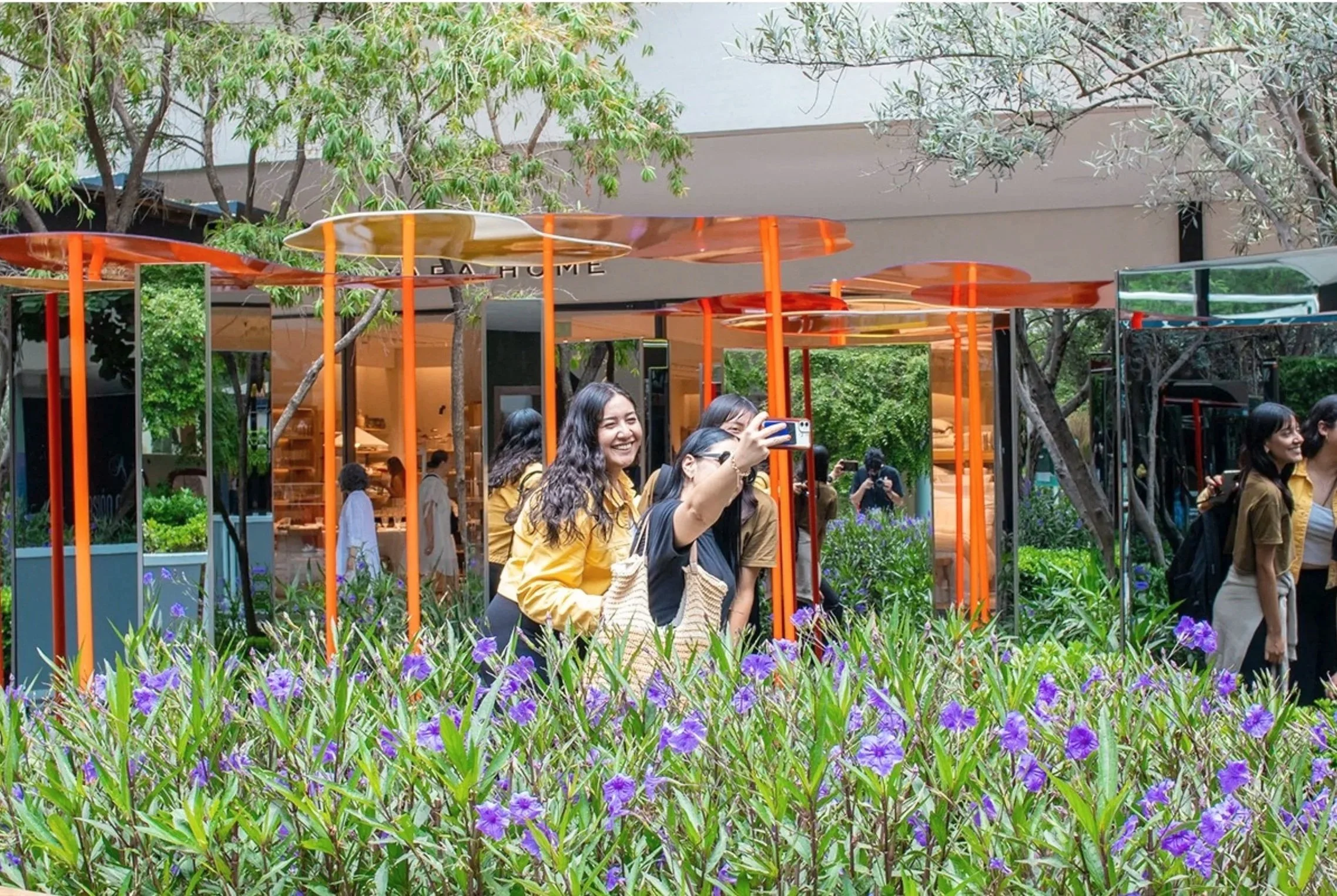 People taking photos and walking in a garden with purple flowers and orange modern architectural structures.