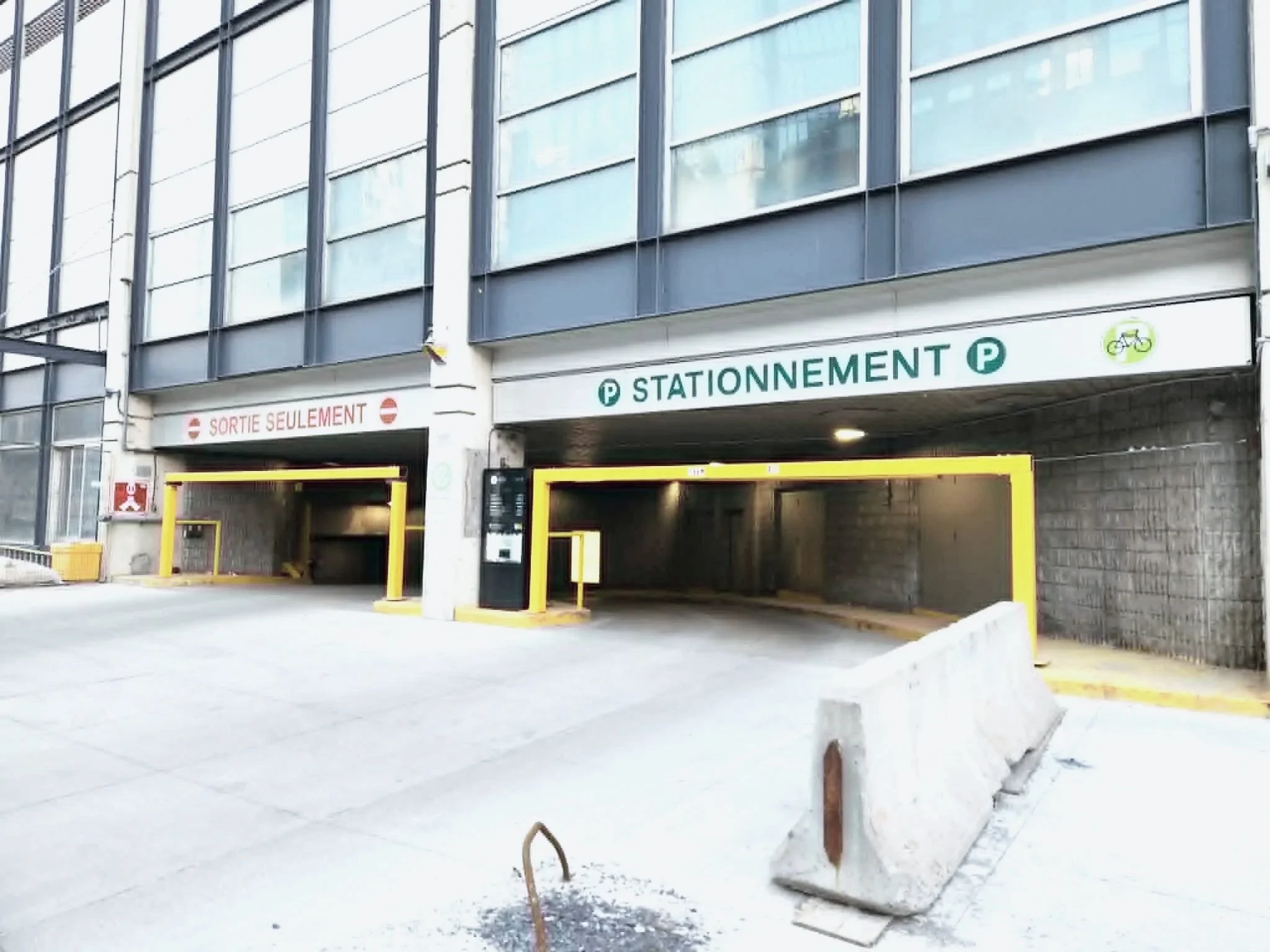 Multistory parking garage entrance with signs indicating 'Sortie Seulement' and 'Stationnement' in French, with yellow barriers and a snow-covered ground.
