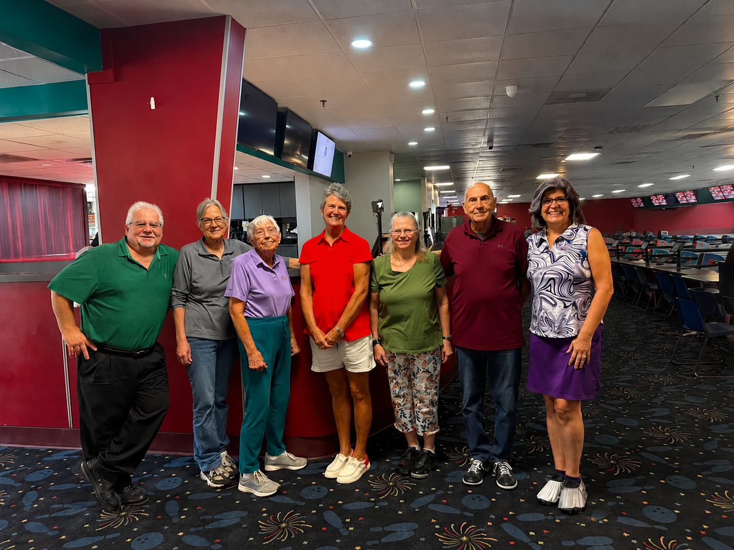 Group of seven people standing in a bowling alley, smiling at the camera.