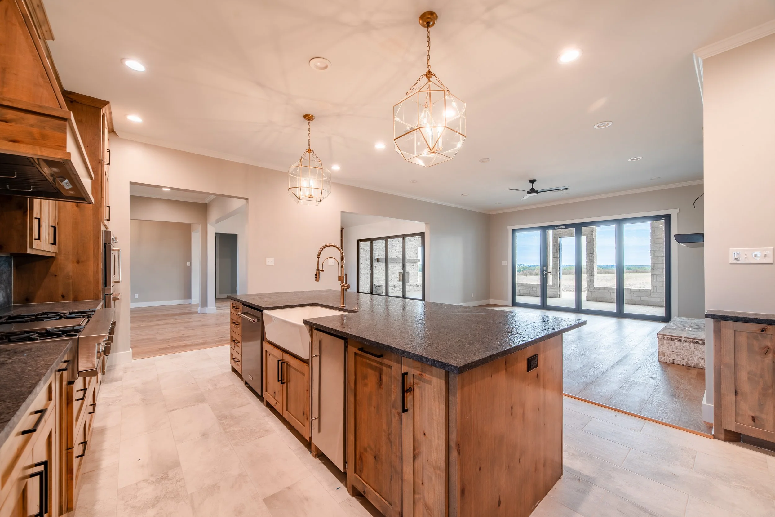 Open-concept kitchen with island, wooden cabinets, granite countertops, pendant lights, and large sliding glass doors leading to an outdoor patio with view of cloudy sky.