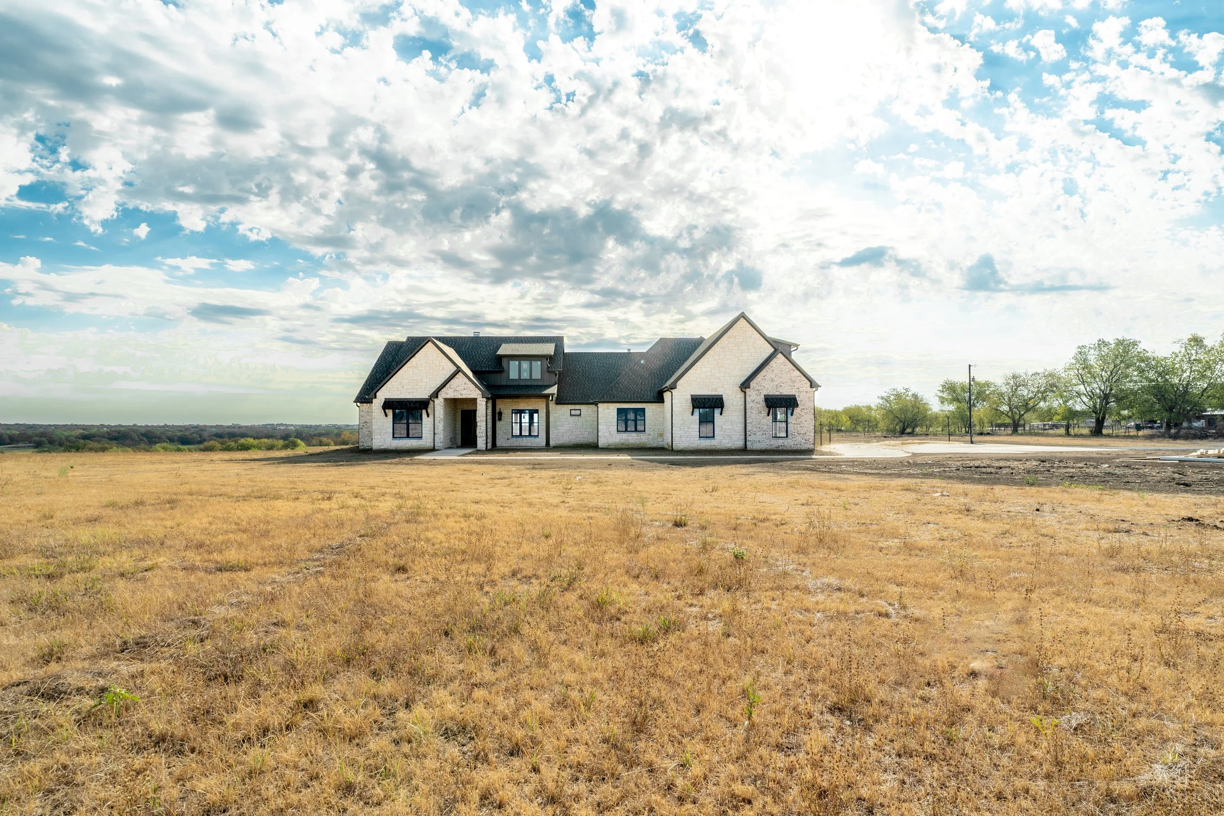 A house under construction in a rural area with a cloudy sky overhead and trees in the background.