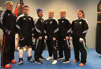 Gruppesbilde av fem personer i idrettsklær og to personer i treningsdresser, med fokus på sportsutstyr og en innendørs treningsarena.