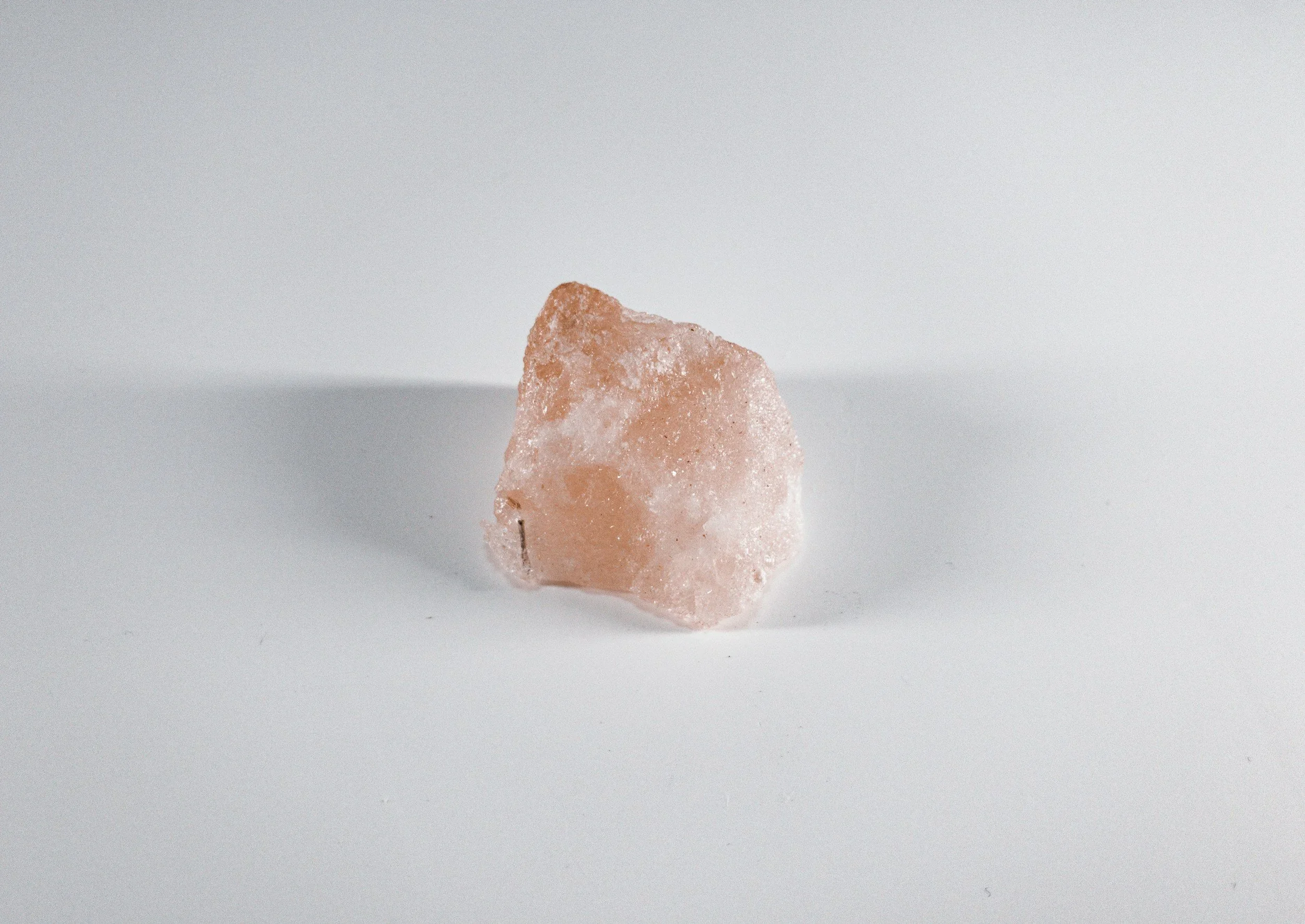 A pink salt crystal against a plain light grey background.