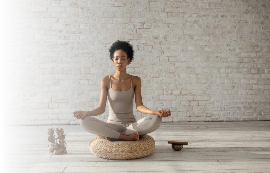 Woman meditating on a cushion in a light-filled studio.
