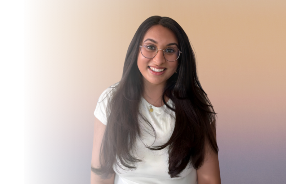 A young woman with long dark hair, glasses, and a white shirt smiling at the camera against a gradient beige and pink background.